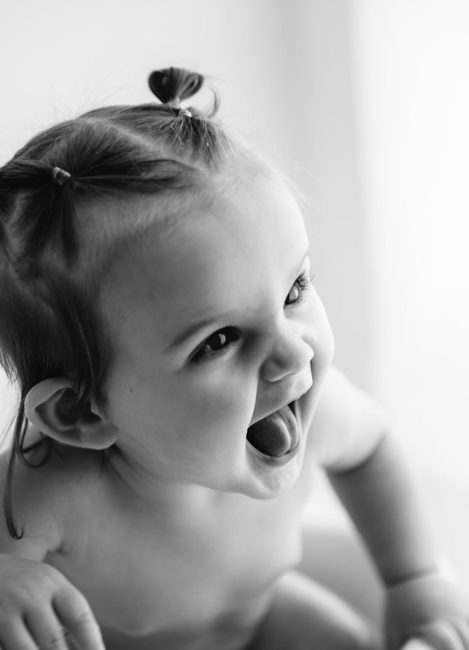 Black and white photo of a laughing baby girl with tiny pigtails, looking up with joy.