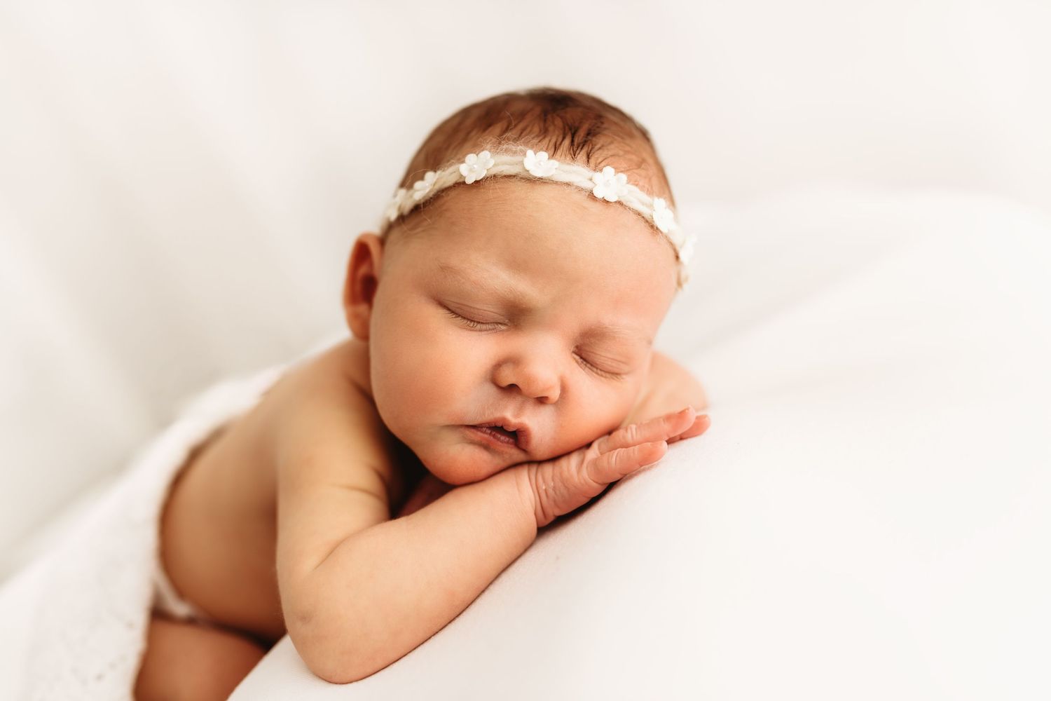 A sleeping newborn baby lies peacefully curled up in soft white fabric during a professional photography session.
