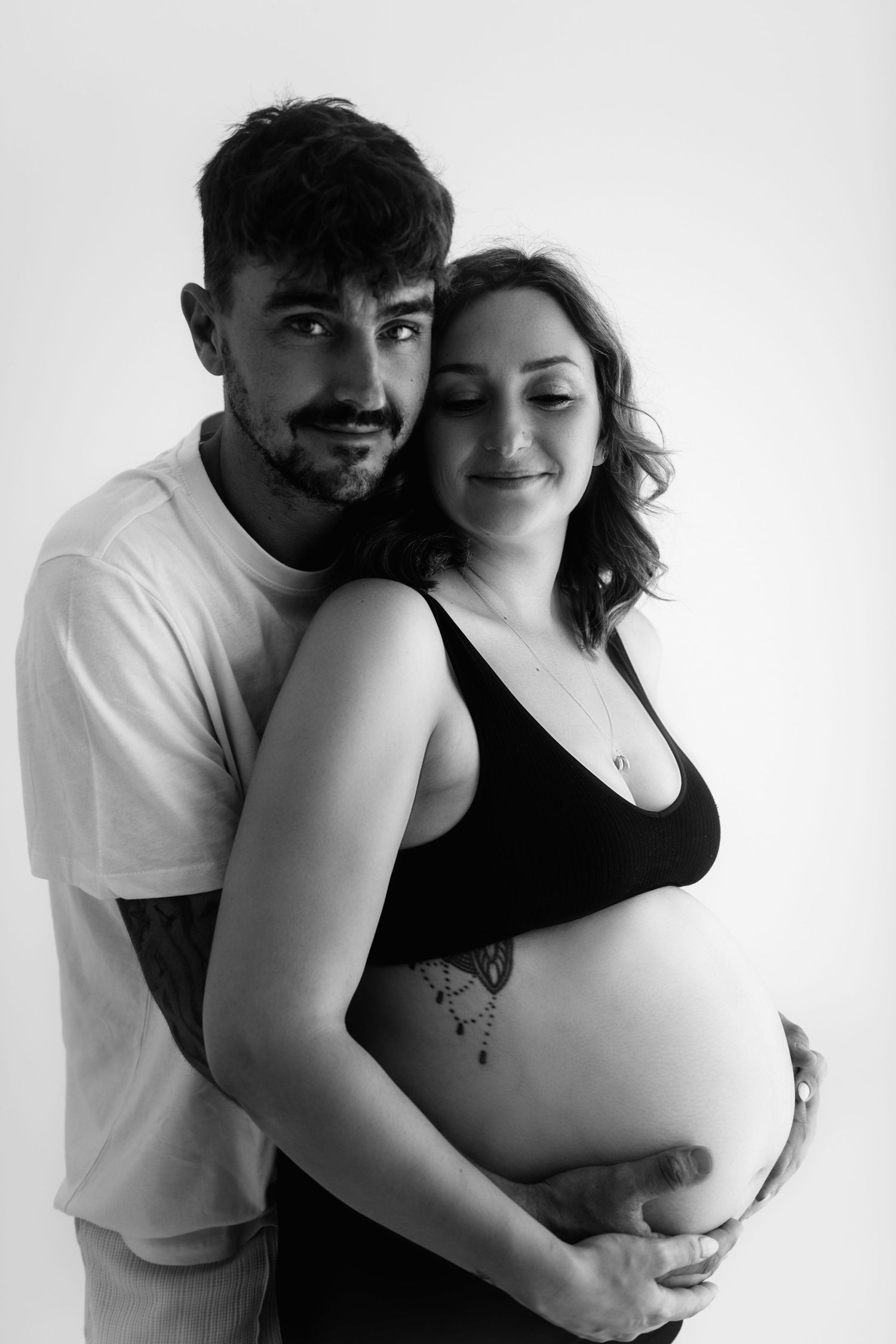 Intimate maternity photoshoot showing couple embracing against white backdrop.