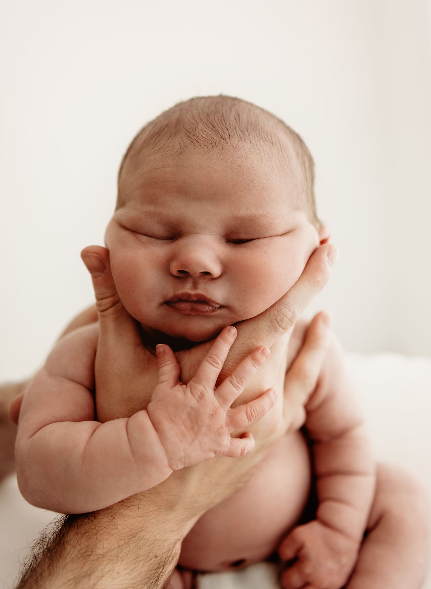 Close up of sleeping newborn baby being gently cradled in hands against white background.