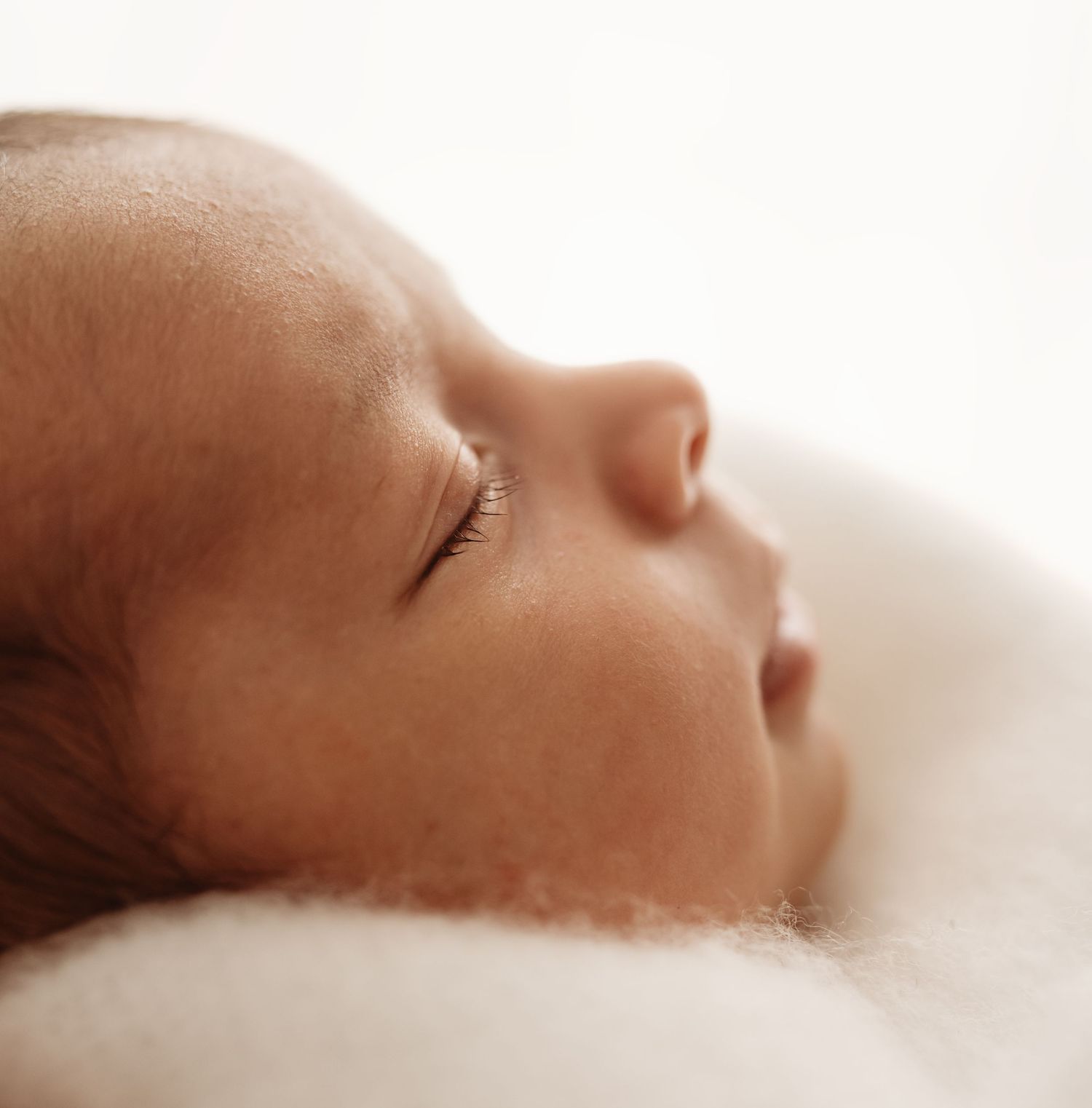 Close-up profile of a sleeping newborn baby resting peacefully on a soft white blanket.