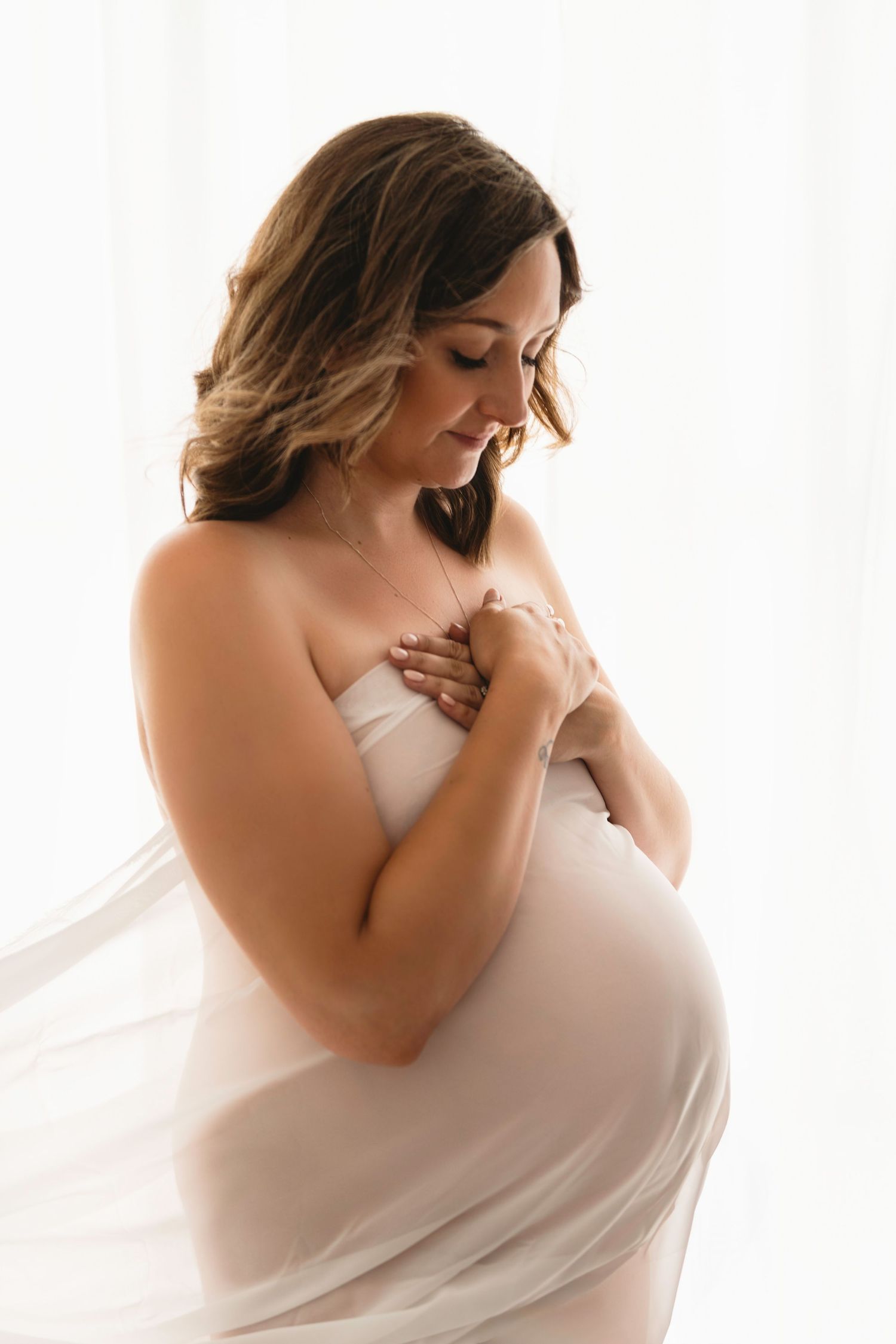 Ethereal maternity portraits with woman draped in flowing white fabric.