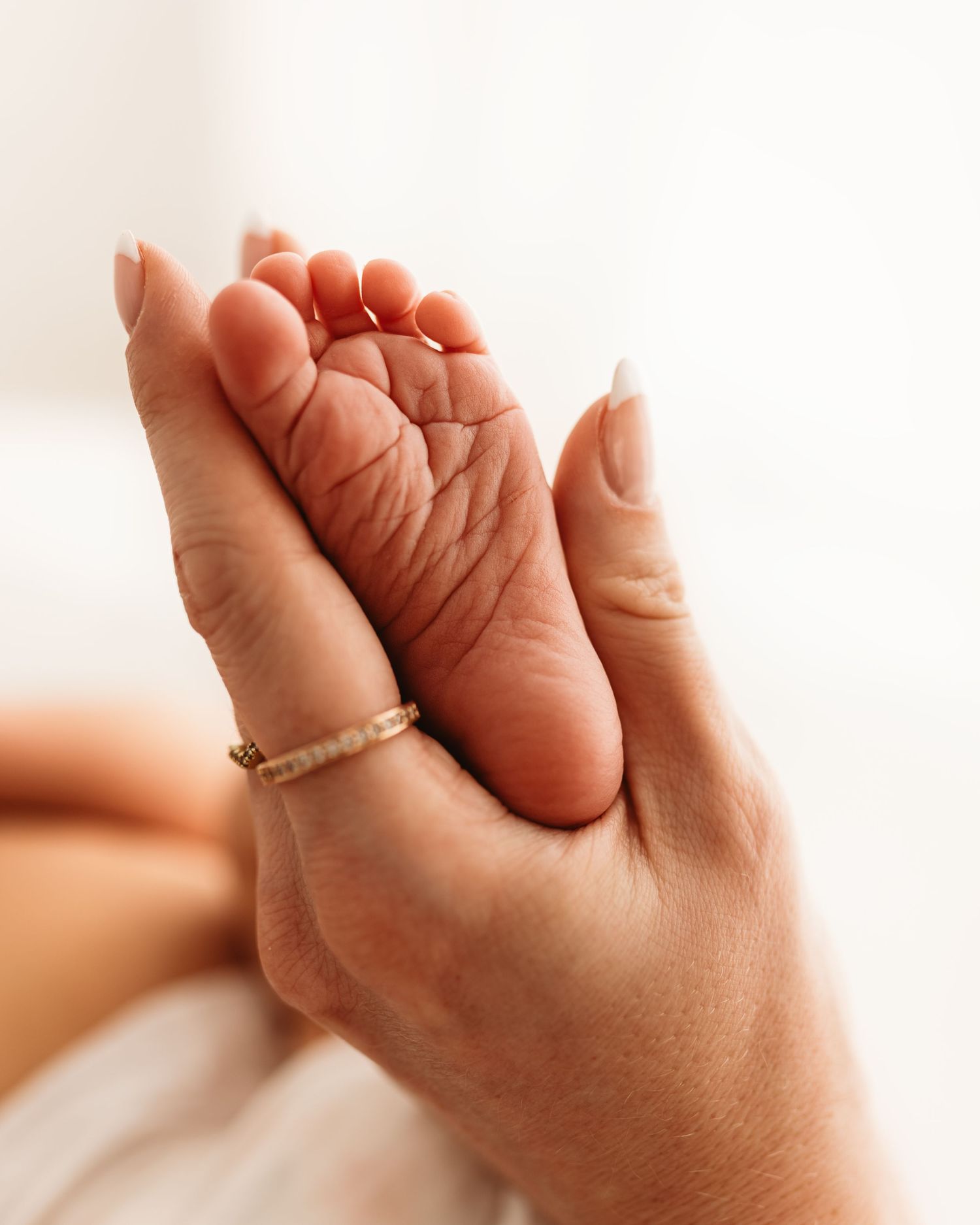 Adult hand with gold ring gently cradling a newborn baby's tiny foot in a tender, close-up portrait during a newborn photoshoot