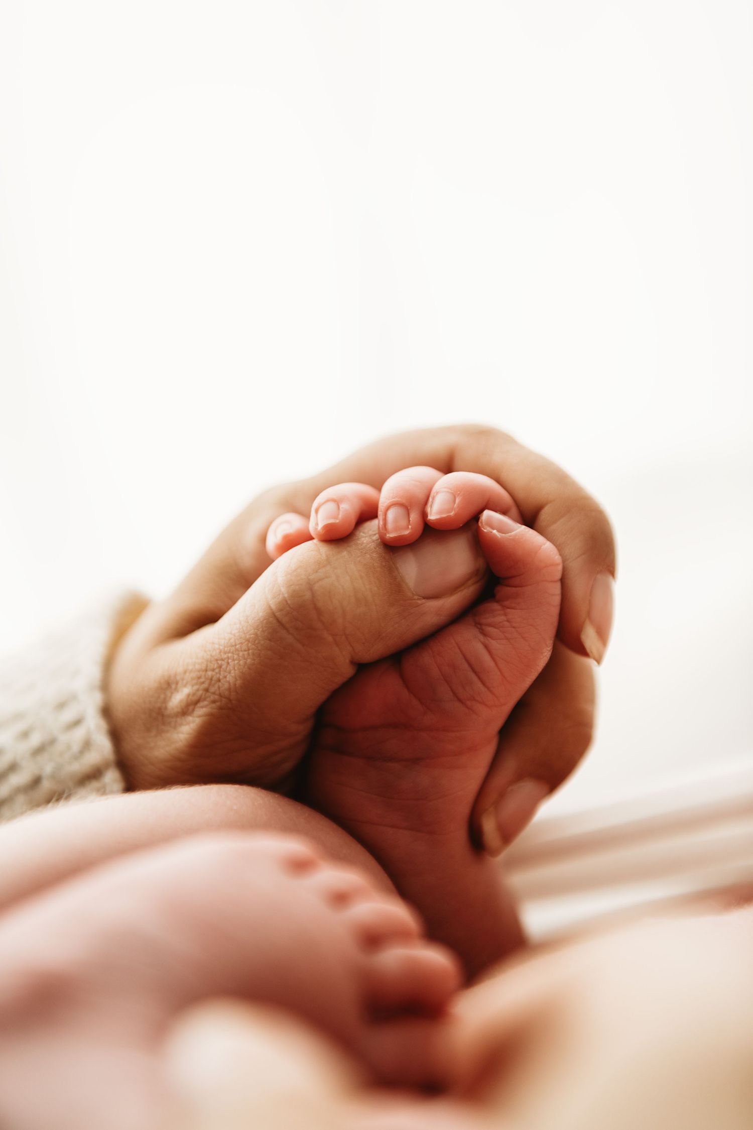 Close-up view of baby's tiny feet against soft white bedding in gentle natural light.