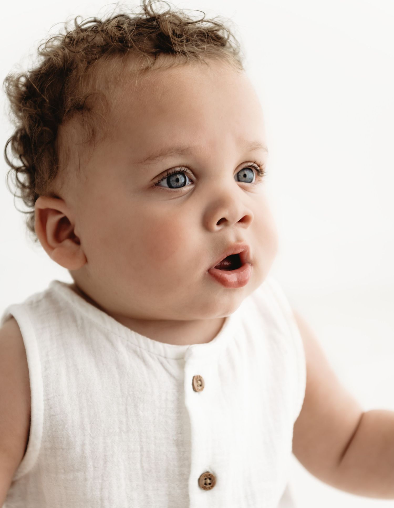 Three artistic black and white portraits of a baby wearing white clothing with wood buttons against a light background.