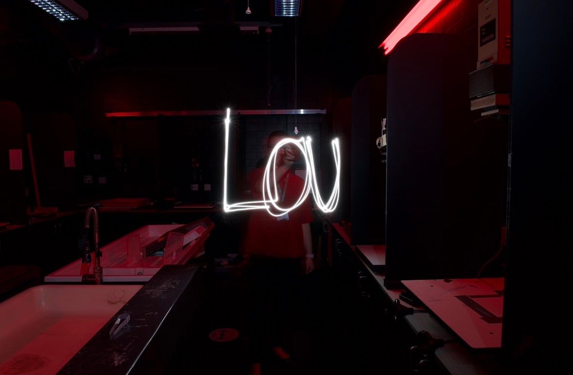 Neon sign spelling Lou glowing in white light against a dark moody bar interior with red accents.