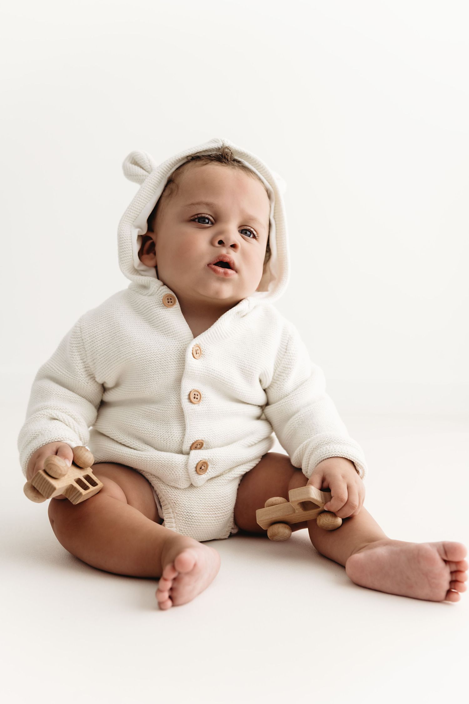 Baby wearing cream-colored knit cardigan sits against white background in four progressive poses showing different angles.