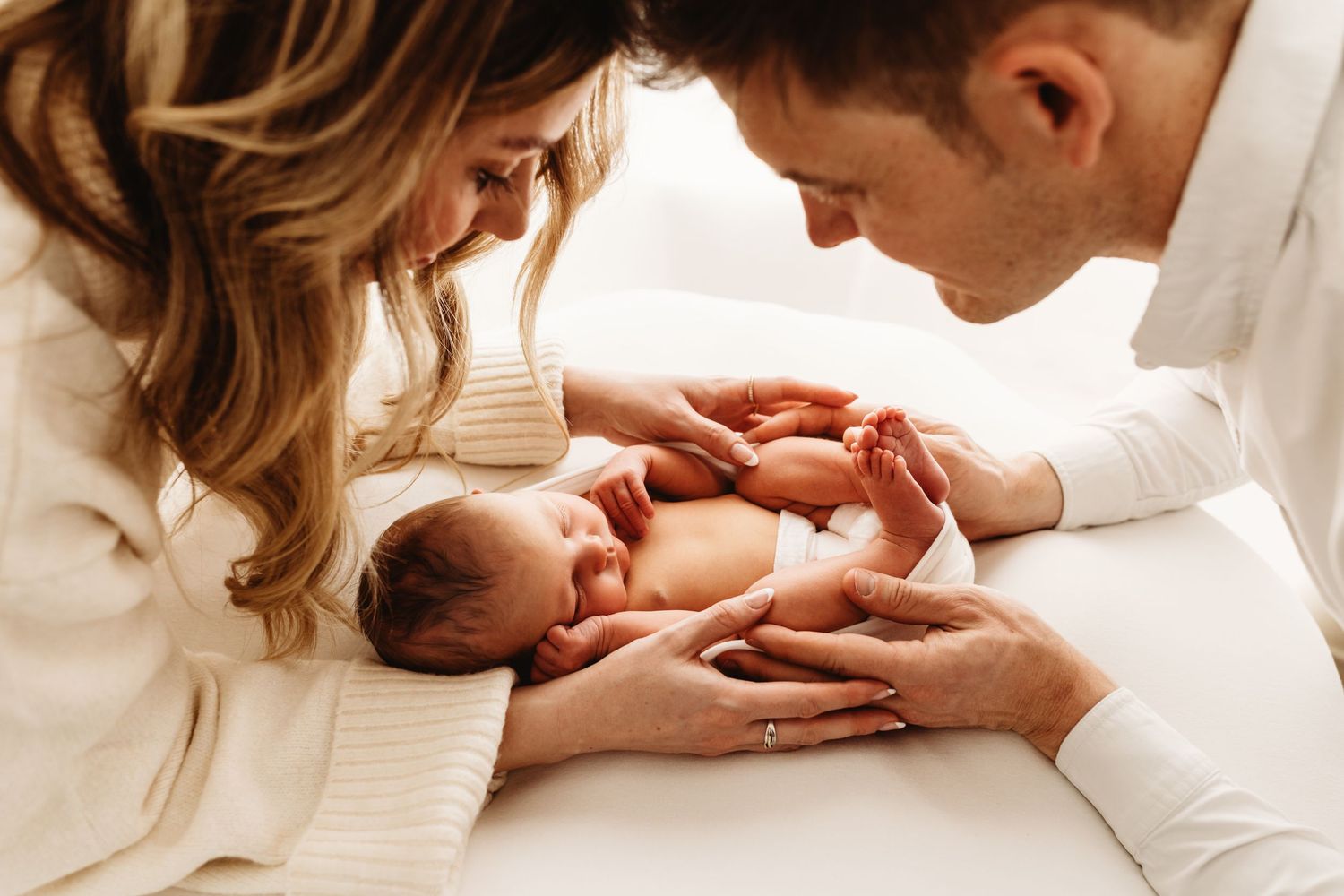 New parents tenderly holding their sleeping newborn baby together, sharing a loving family moment.