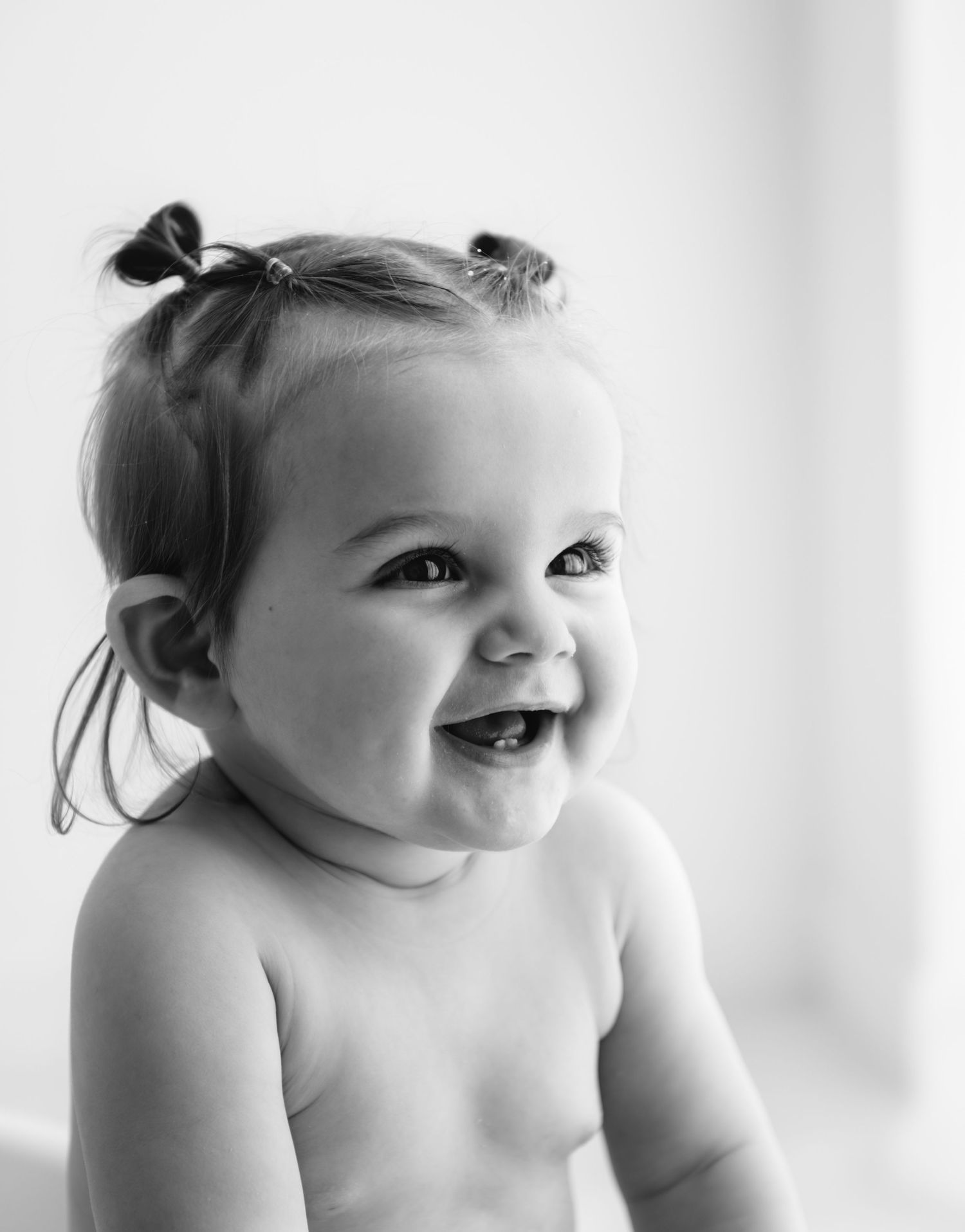 Black and white portrait of a laughing baby with tiny pigtails, showing pure joy and innocence.