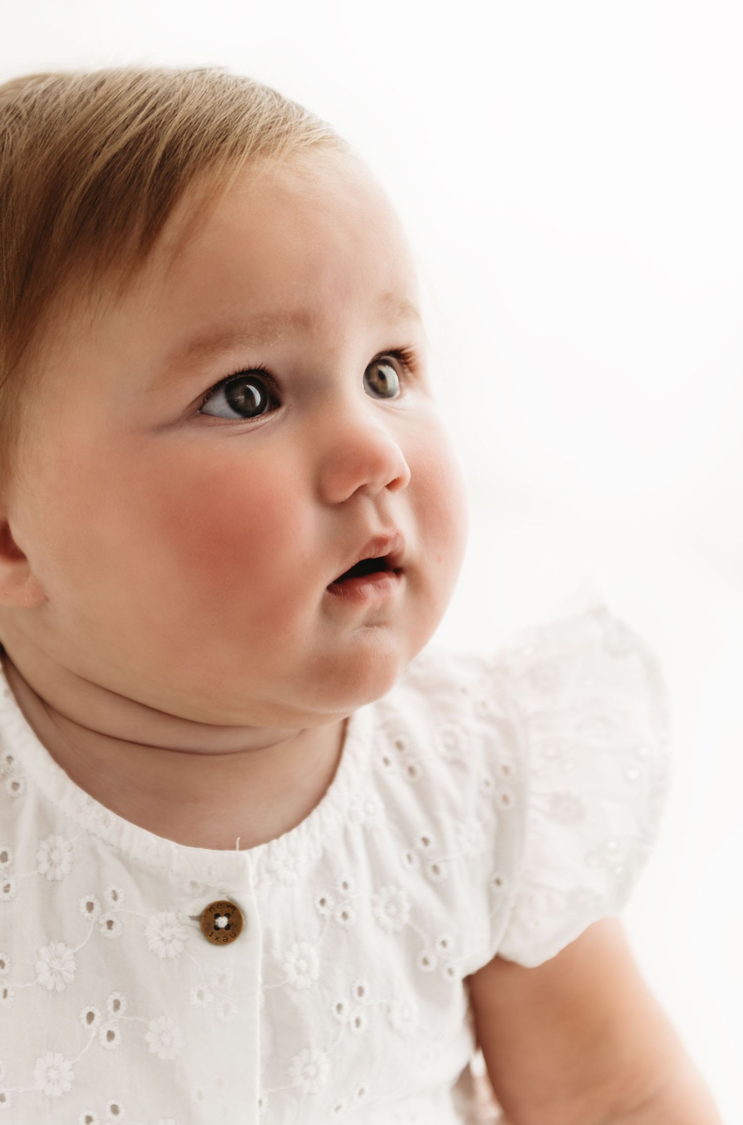 A collage of four close-up shots shows an infant in a white eyelet dress looking upward with different facial expressions.