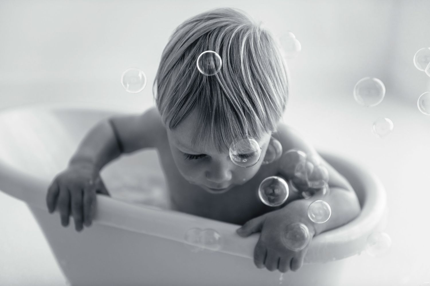Child in bathtub with soap bubbles in dreamy black and white photography.
