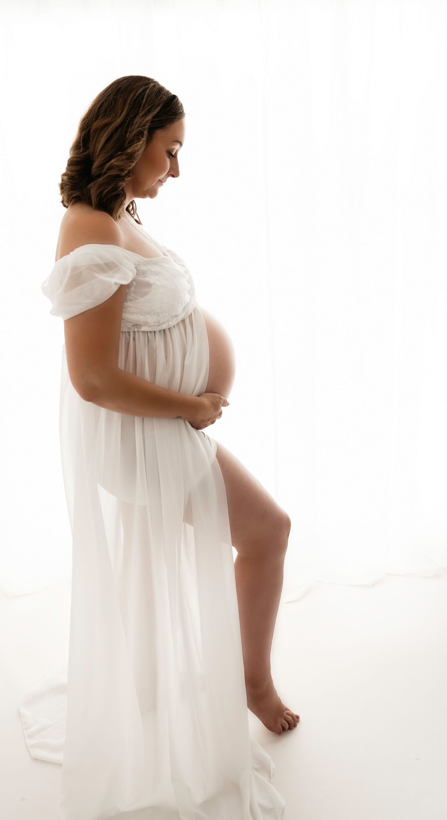 Maternity photos featuring flowing white dress poses against bright background.