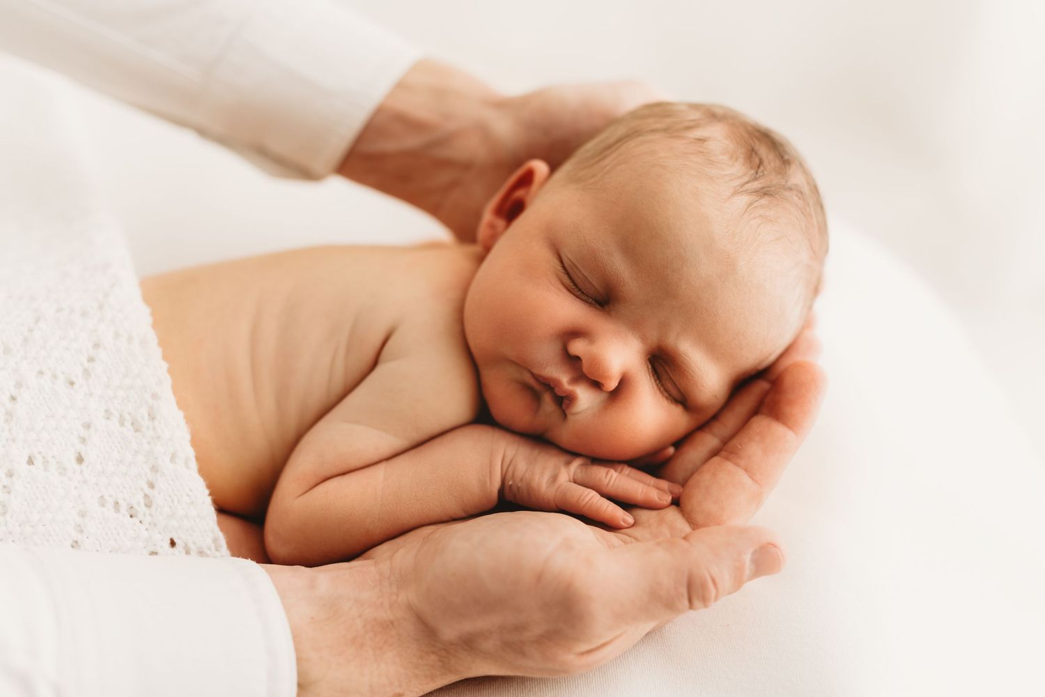Newborn baby sleeping peacefully in adult hands, soft white background, tender newborn photography.