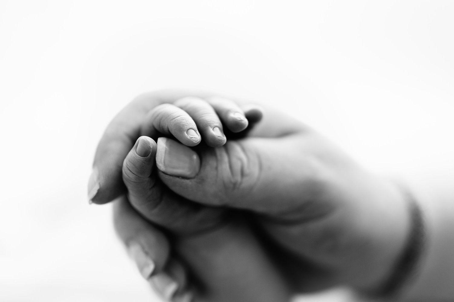 Black and white close-up of a newborn baby's tiny hand gently gripping an adult's finger.