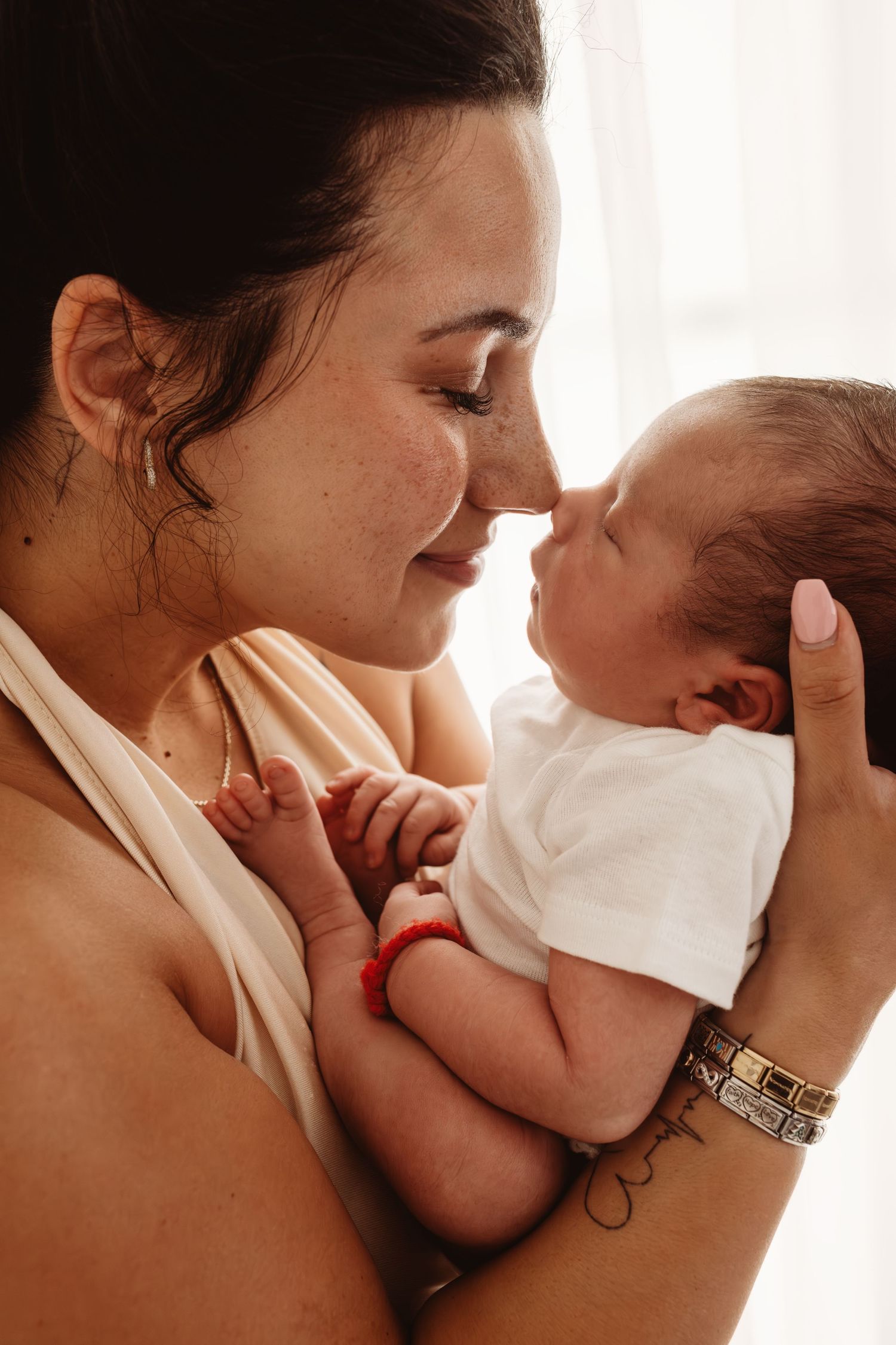 A young mother with freckles tenderly touches noses with her newborn baby, sharing a sweet bonding moment.