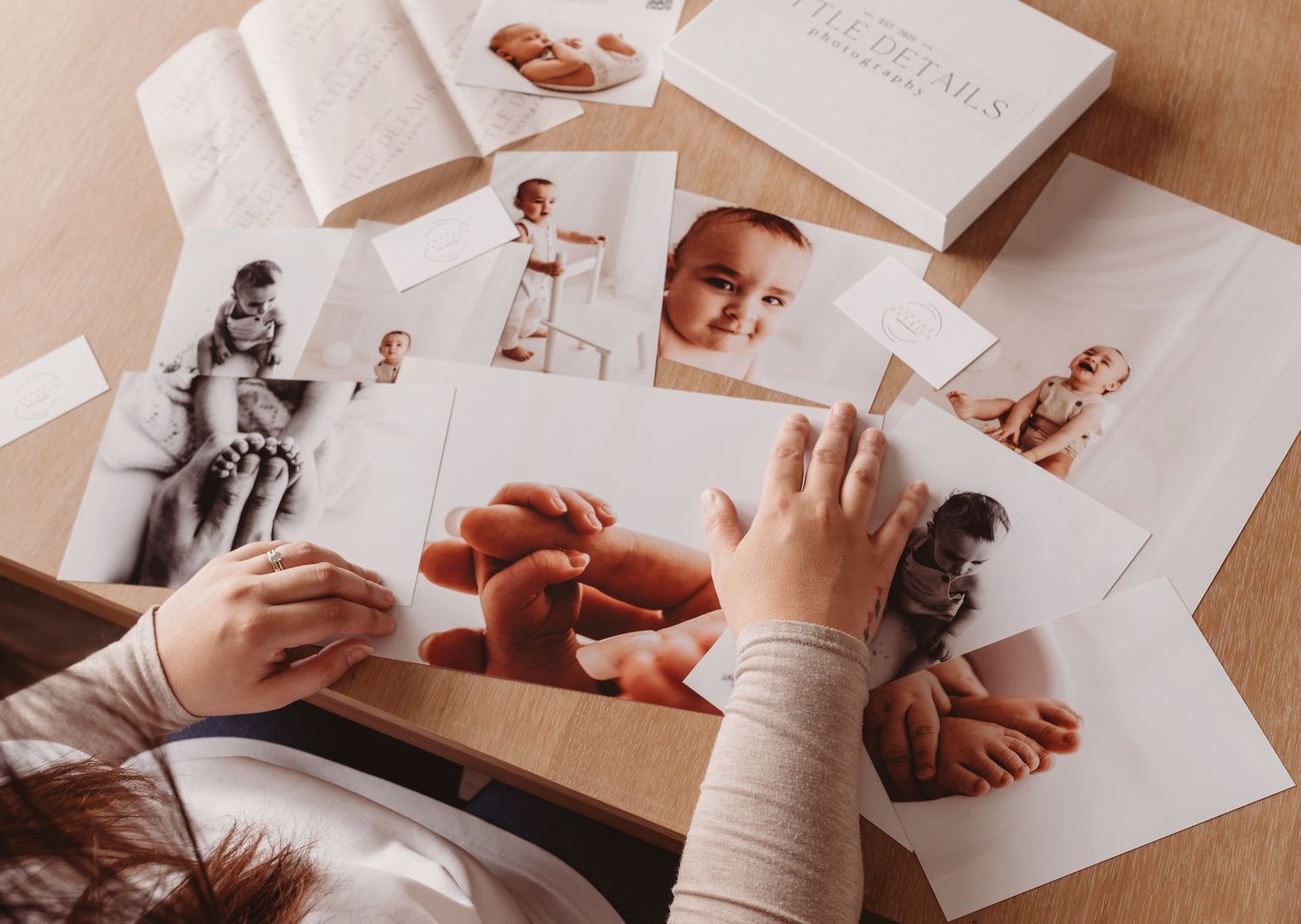Person sorting printed baby photos on a wooden table, including newborn and infant portraits in color and black and white.