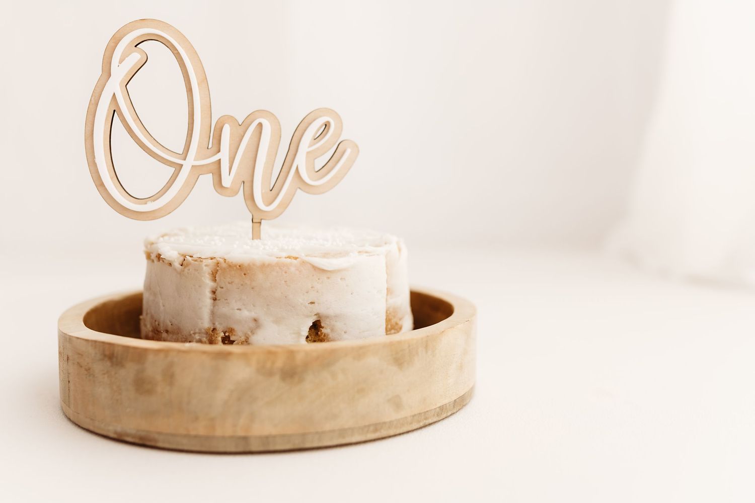 A small smash cake with a gold 'One' topper displayed in a wooden bowl for a first birthday celebration.