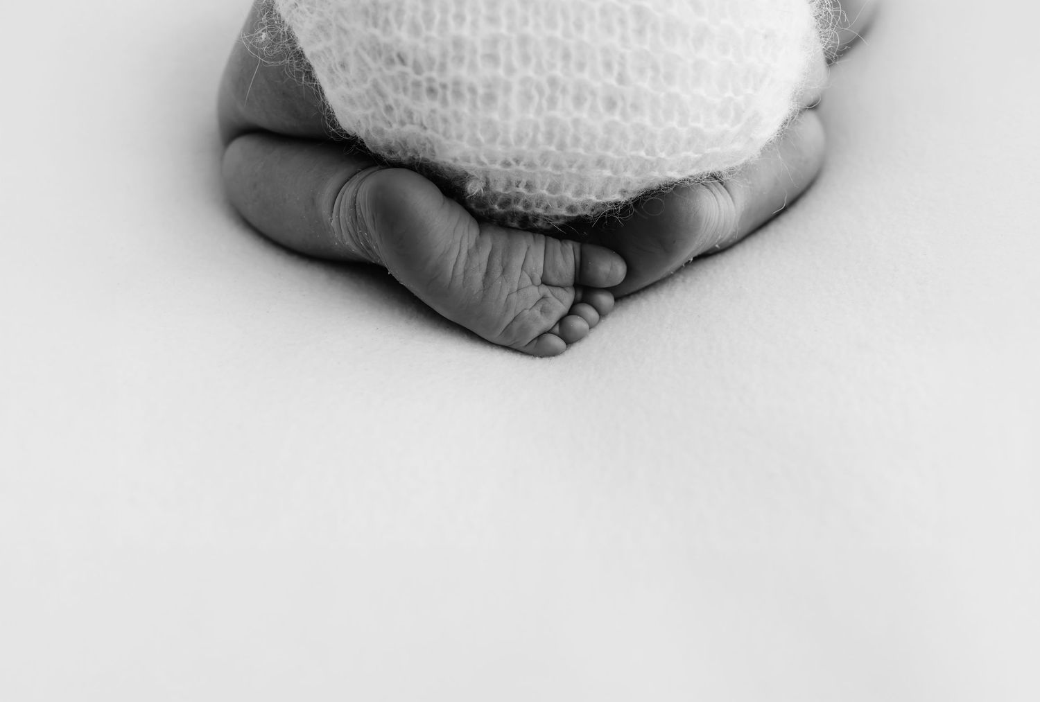 Black and white newborn photography showing tiny baby feet and toes curled up, wearing a soft knit hat.