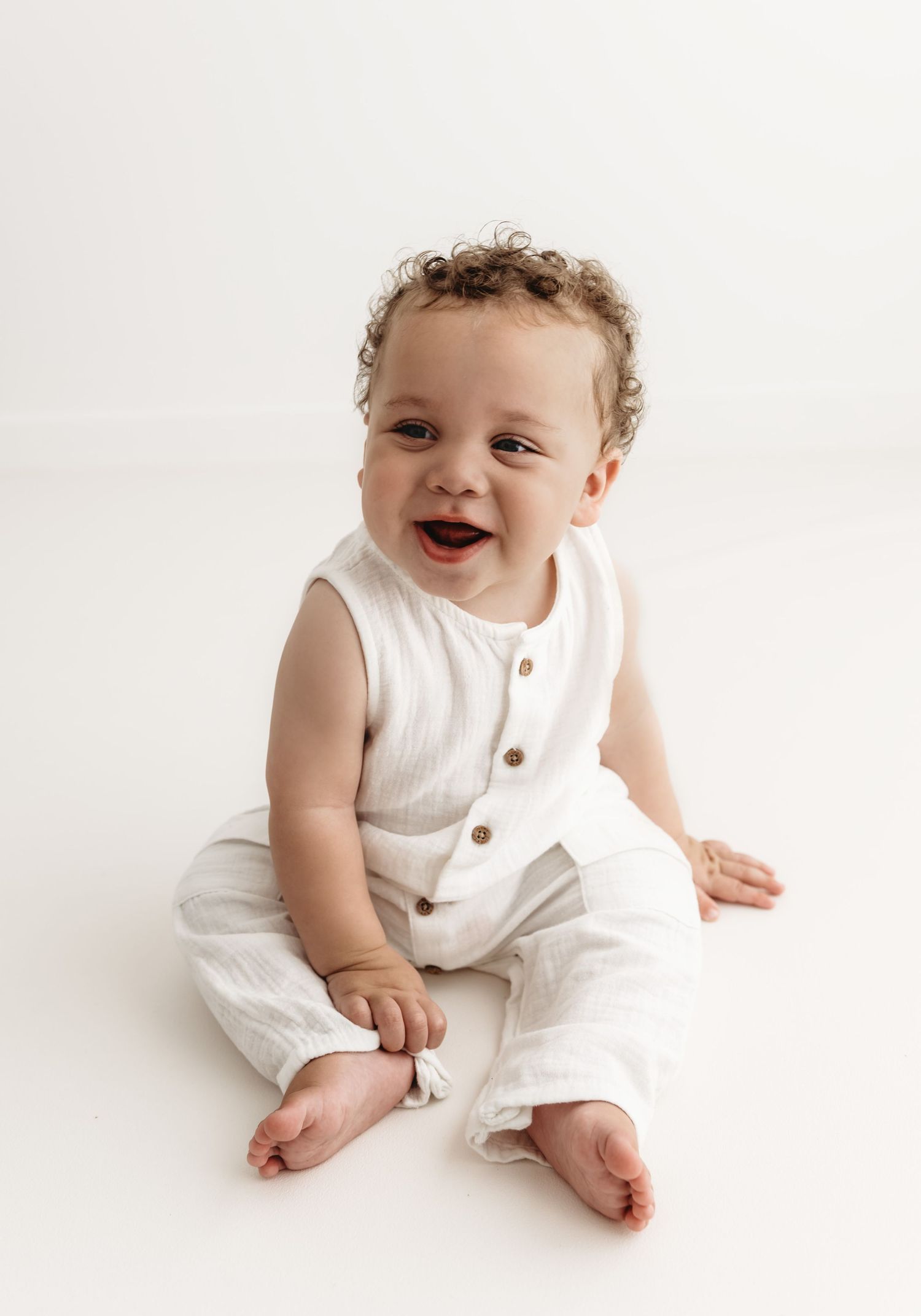 Happy baby wearing white romper sitting and smiling on white background during a Sitter  studio photoshoot in Corby, Northamptonshire
