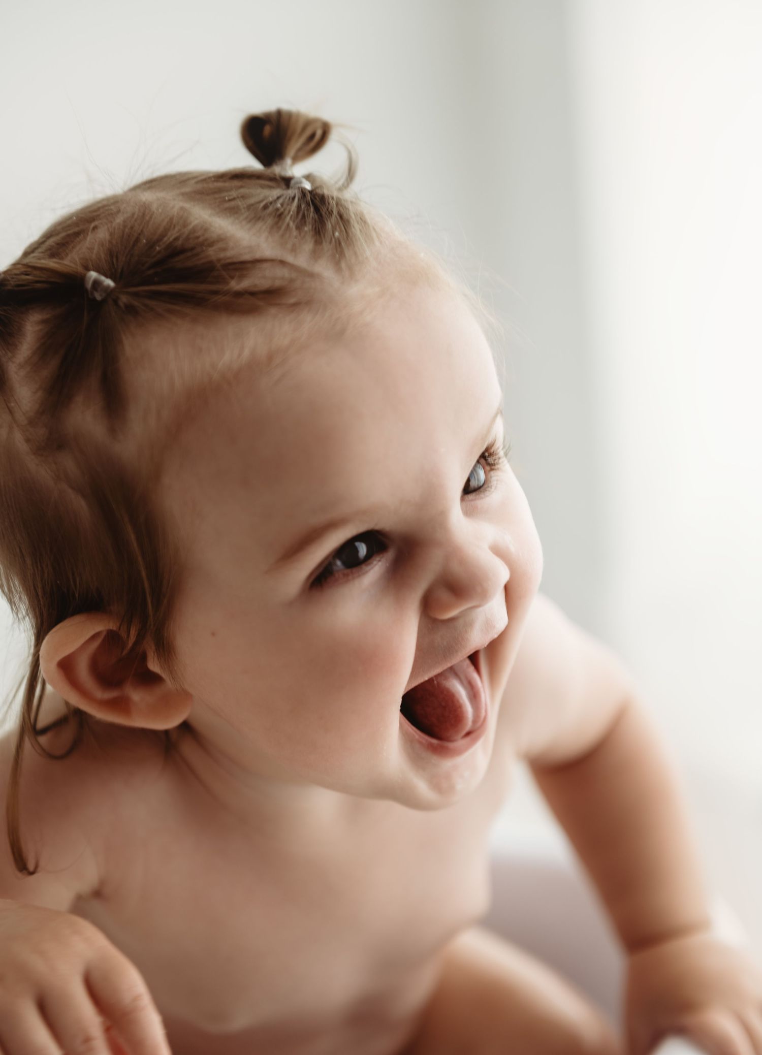 Adorable baby girl with tiny pigtails laughing and leaning forward, showing pure joy and happiness.