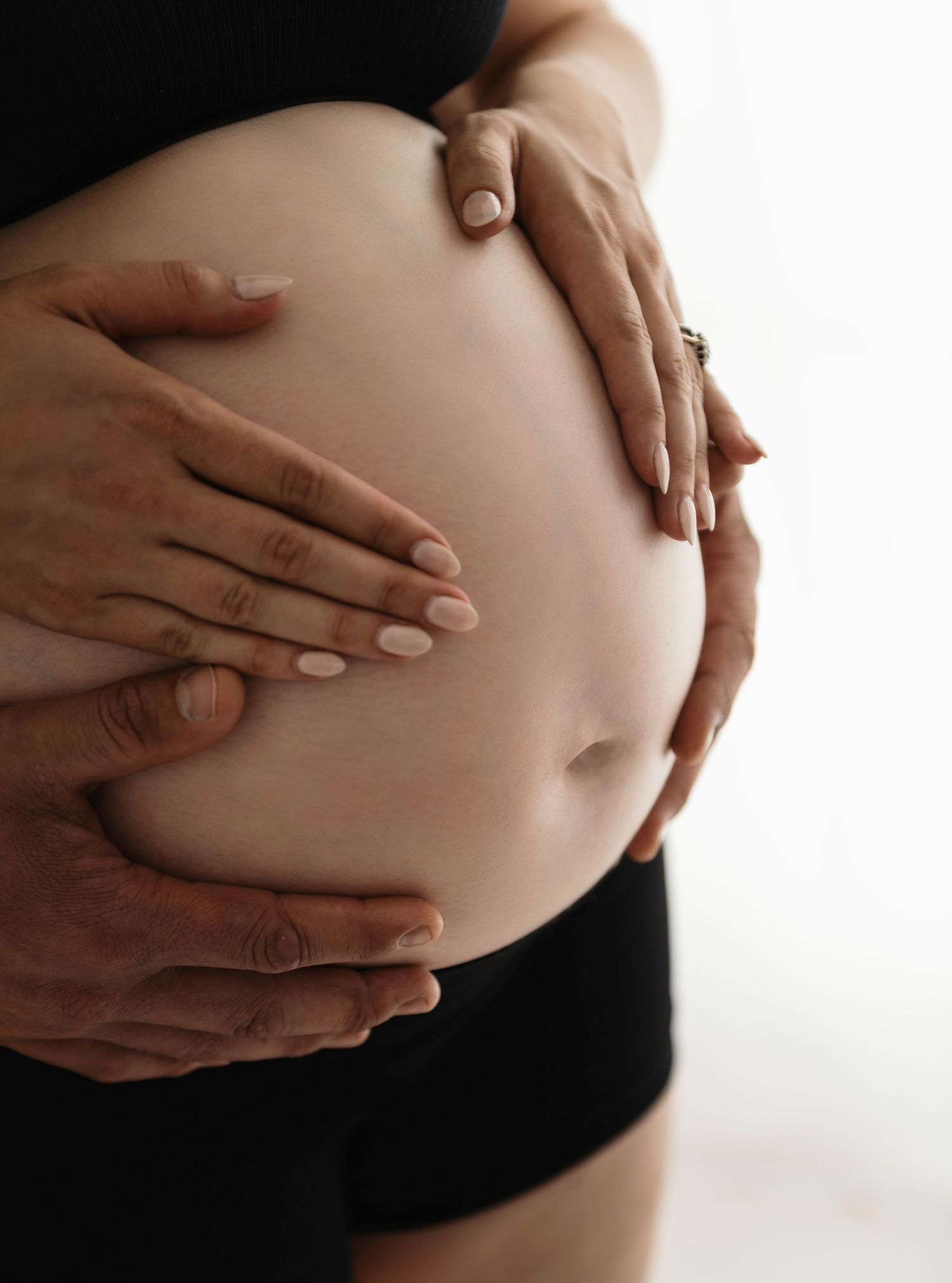Series of hands gently cradling a pregnant belly against white background.