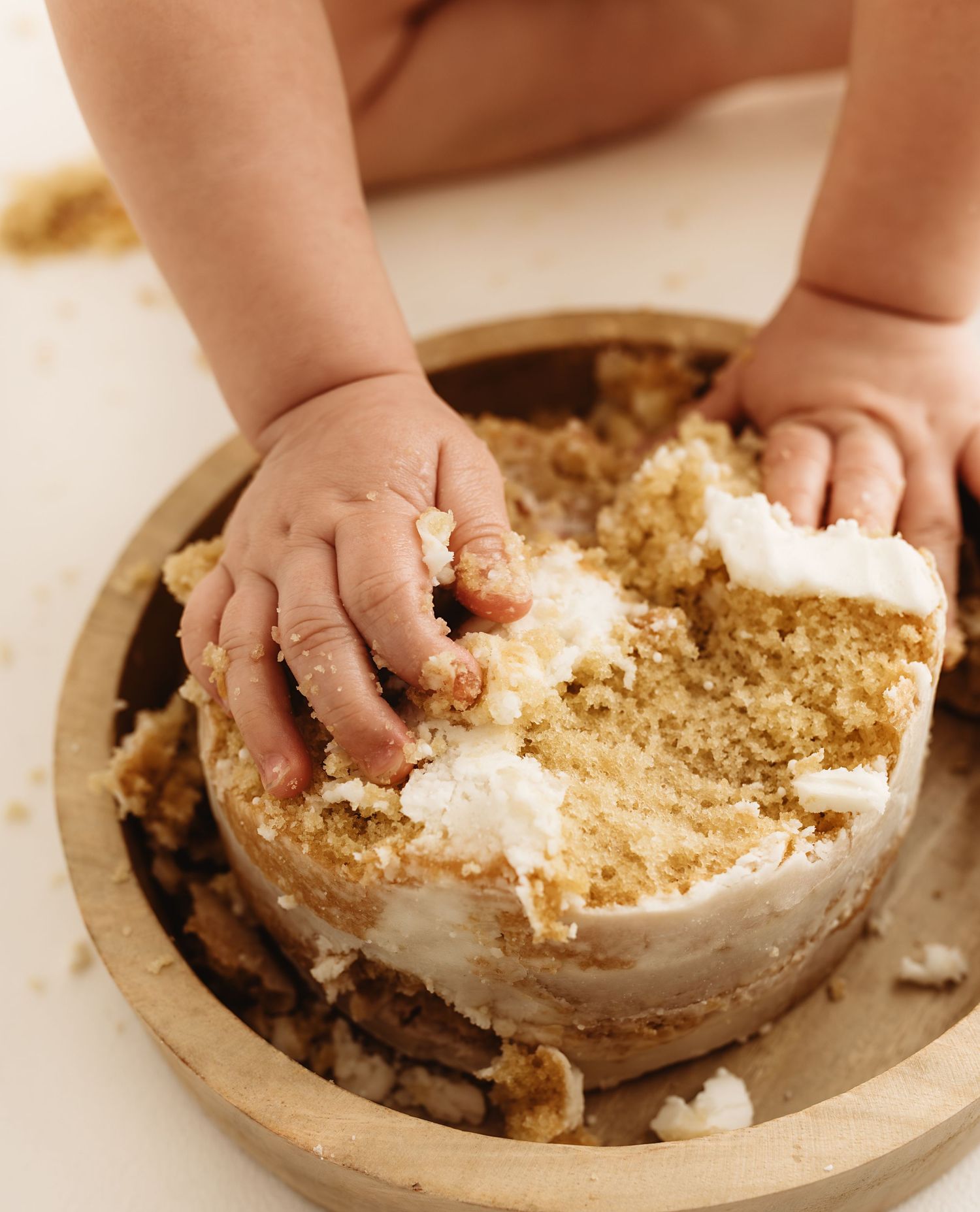 Baby hands smashing into a white frosted golden cake on a wooden plate during a first birthday smash cake session.