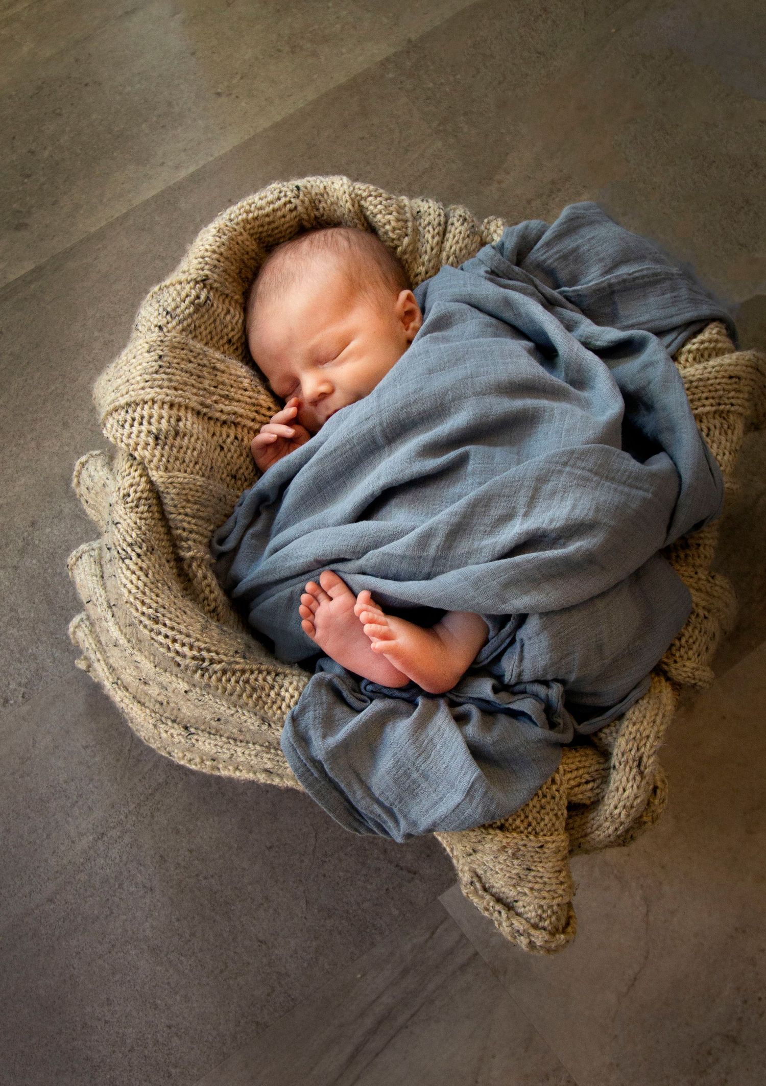 the newborn baby boy is wrapped up in a blue blanket in a basket with brown tones in the background