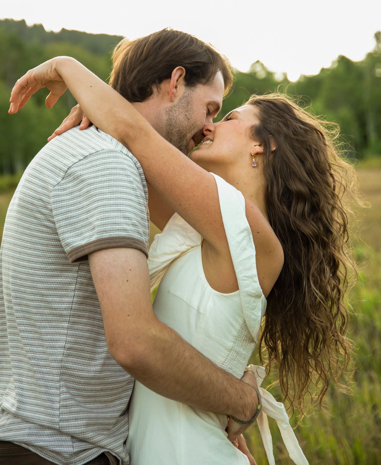 A woman embracing her partner in a gentle, romantic kiss during their engagement photo session in Snowbasin, Utah.