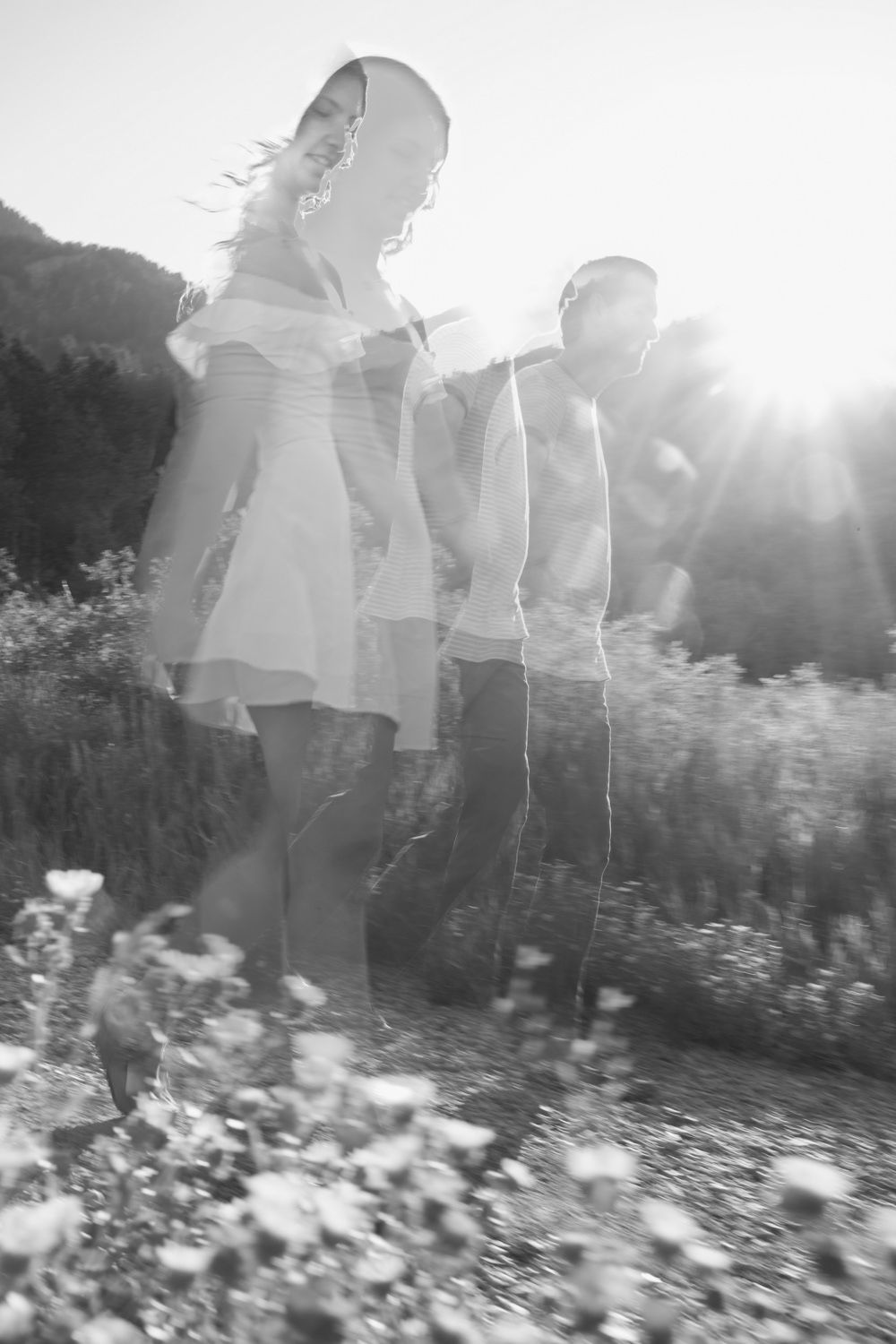 Blurry black and white image of a couple holding hands walking amidst wild flowers.