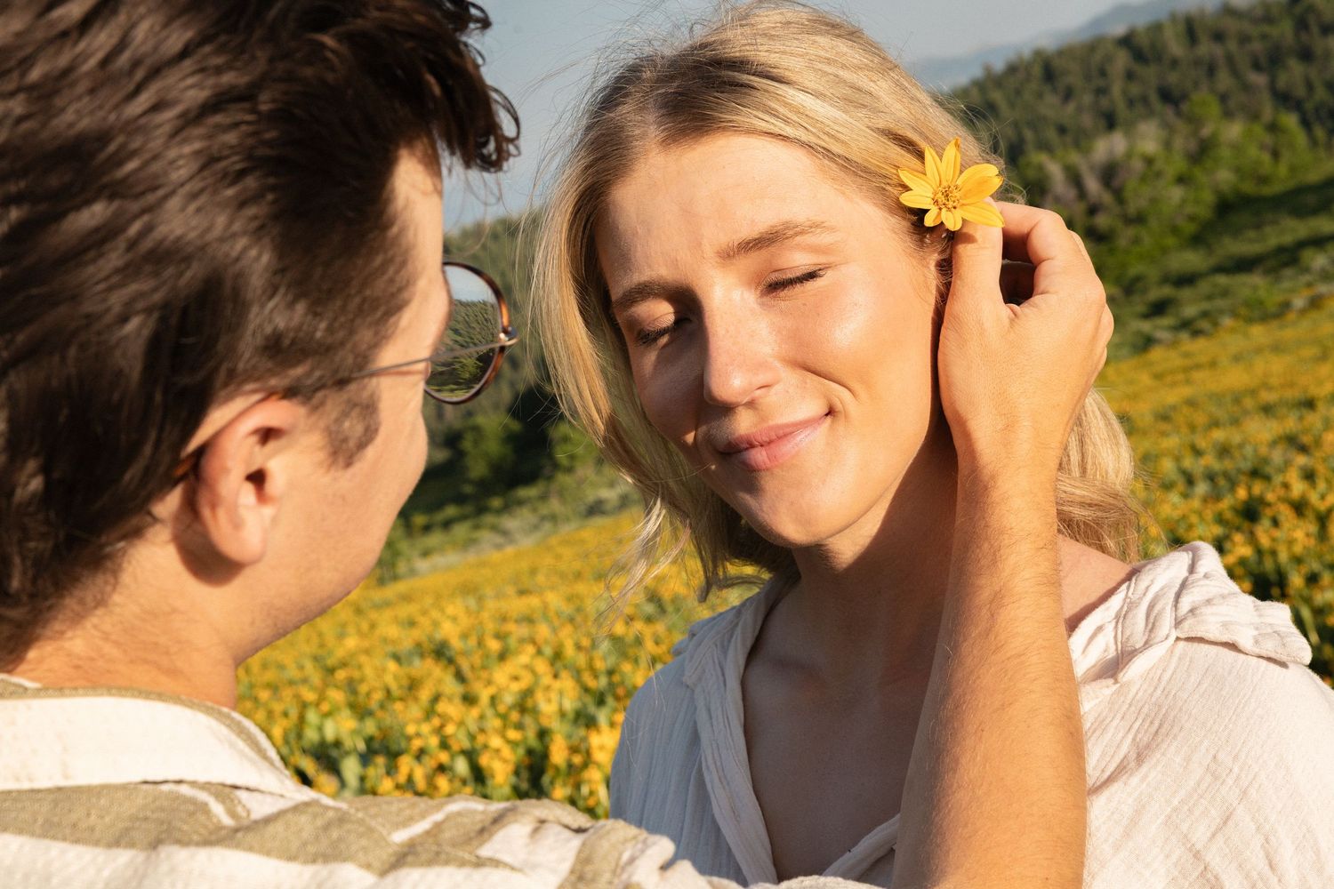 A man tugging a wild flower behind his partner's ear.