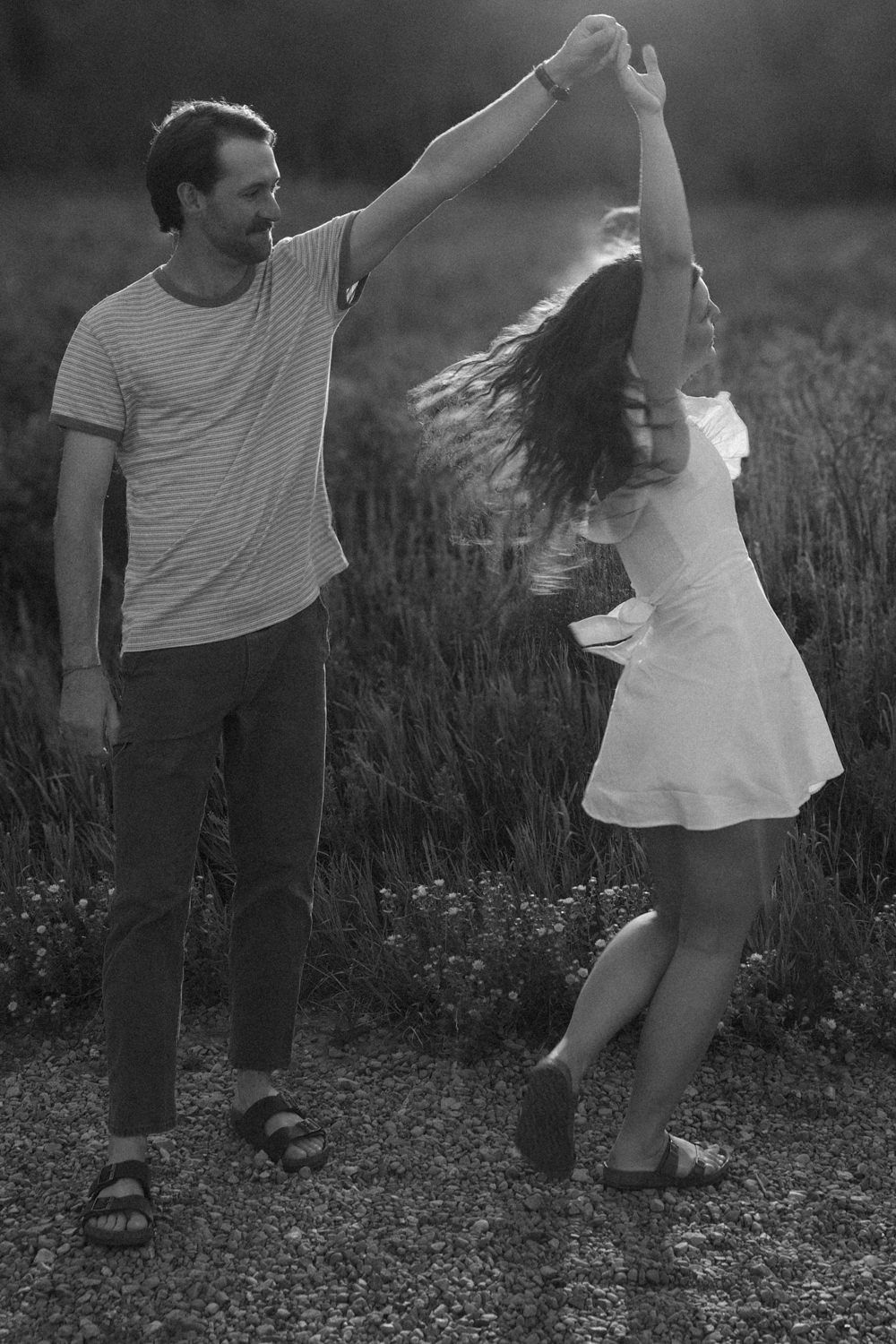 A black and white photo of a couple dancing in the wild flowers.