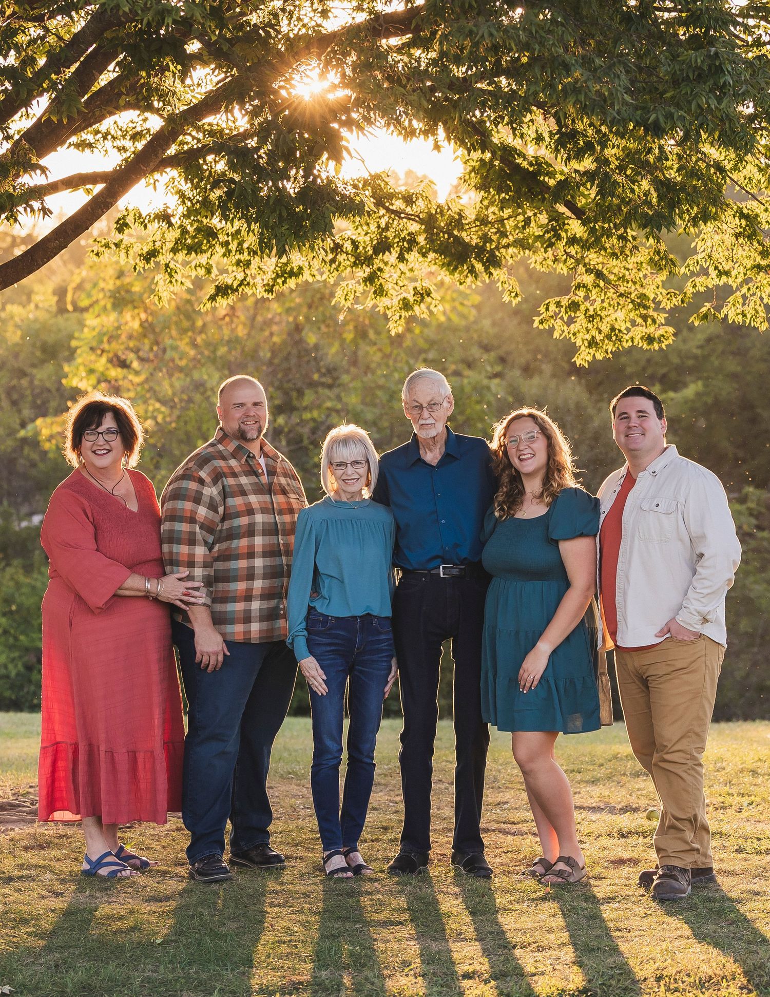 A group stands together in a golden sunlit field during sunset with trees casting long shadows in the background.