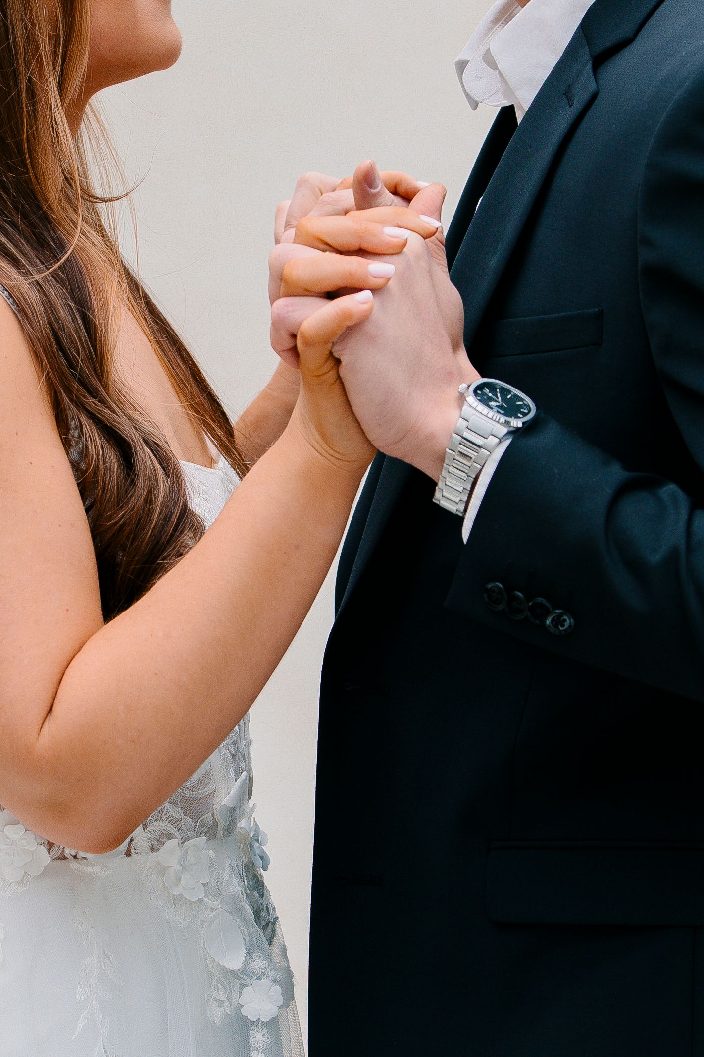 Close-up view of hands holding each other during a wedding ceremony, with a white dress and dark suit visible.