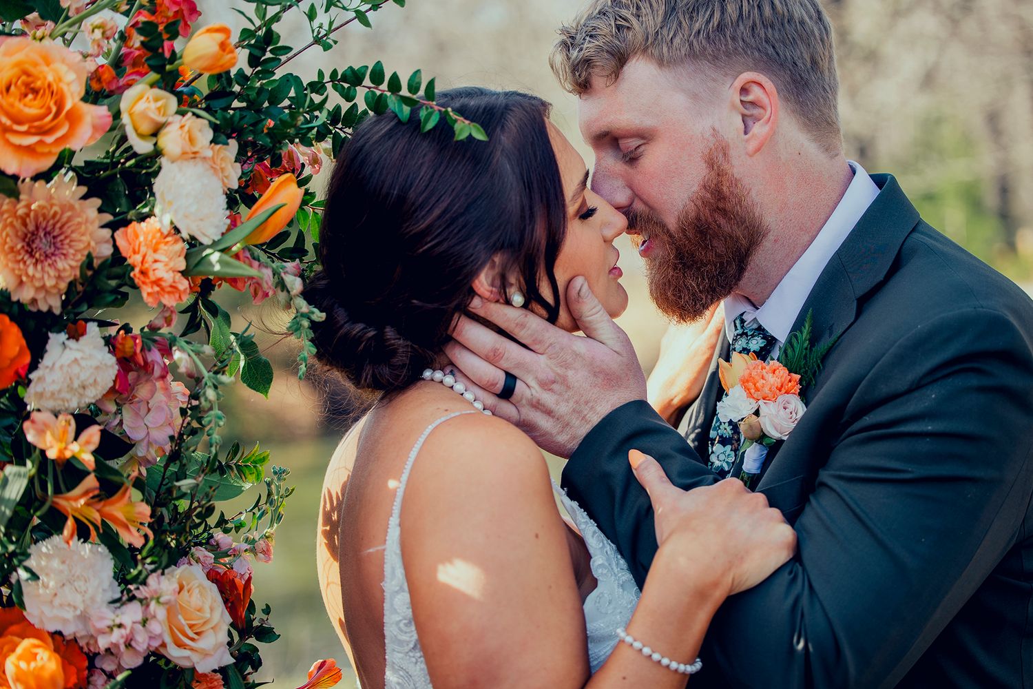 Couple sharing a romantic moment surrounded by vibrant orange and pink floral arrangements at their outdoor wedding.