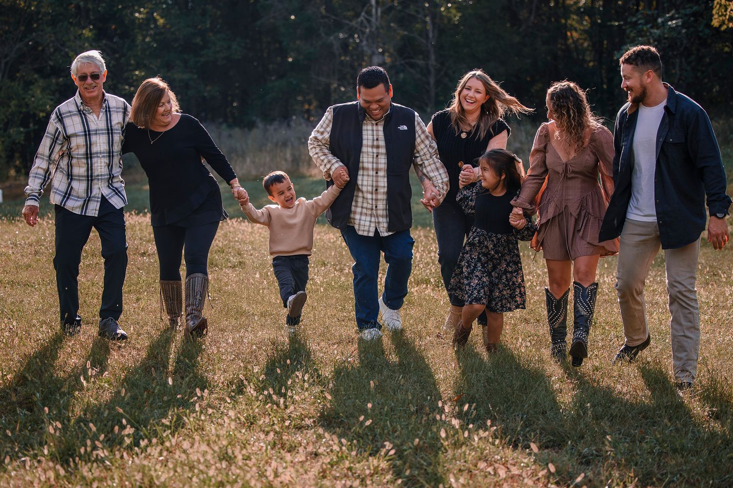 Multi-generational family walking together in a sunlit meadow, smiling and holding hands outdoors.