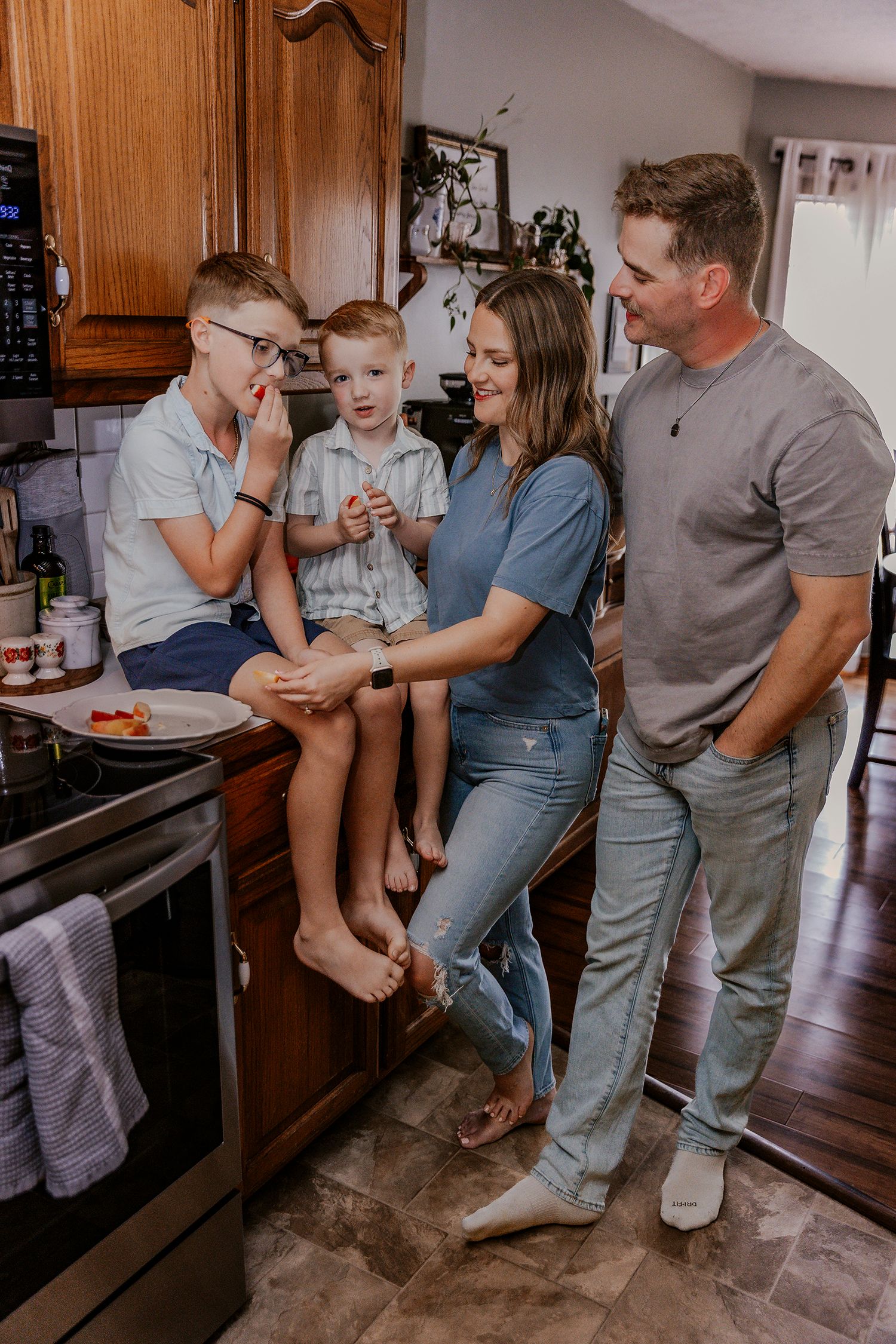 A happy family of four shares a warm moment in their kitchen, with two boys sitting on the counter while parents smile nearby.