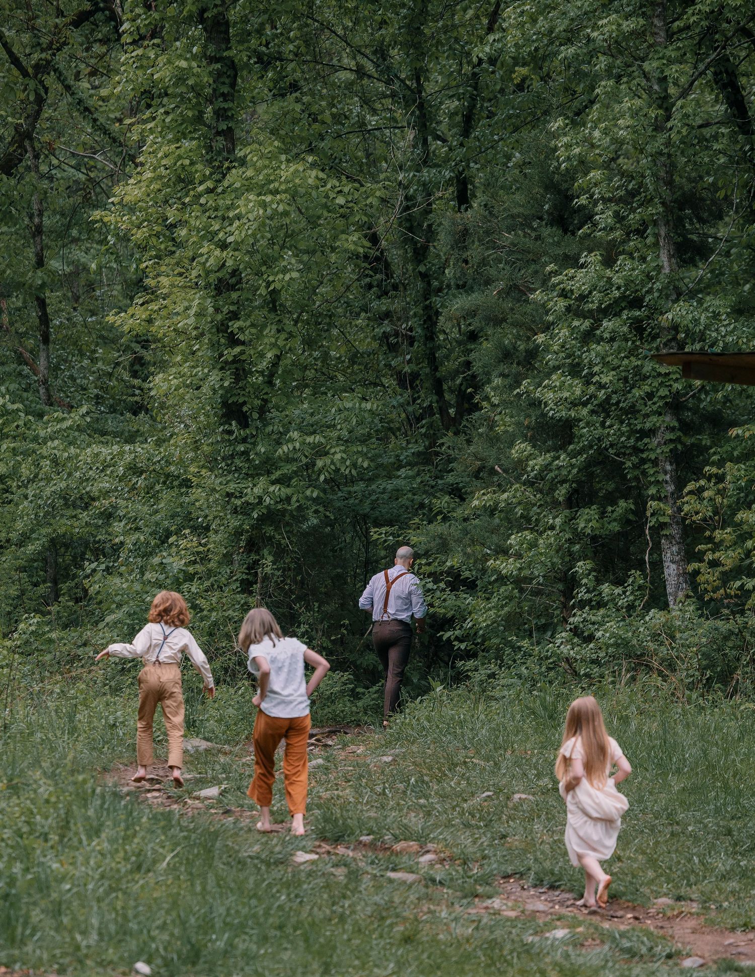 Children running toward an adult on a forest trail surrounded by lush green trees in a serene woodland setting.