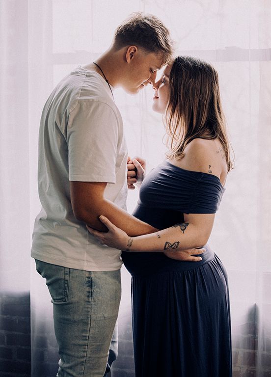 A romantic intimate moment captured between a couple as they stand close together, with her wearing a navy dress.