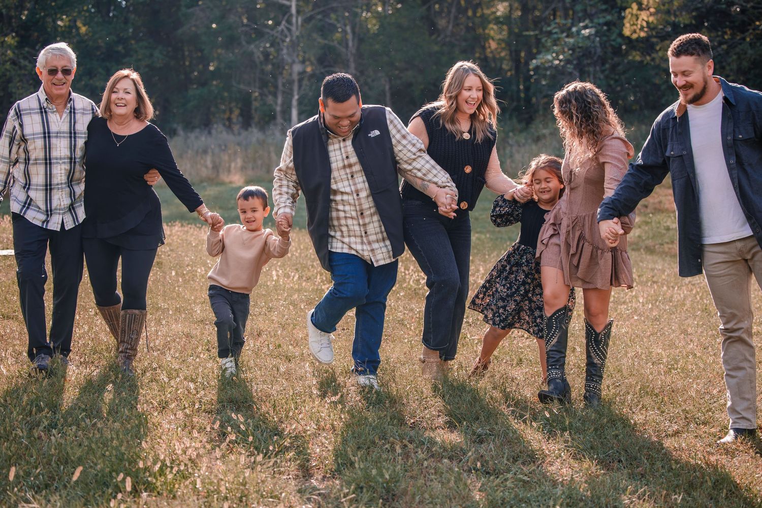 A group of people walking in a line through a golden autumn field at sunset holding hands and smiling.