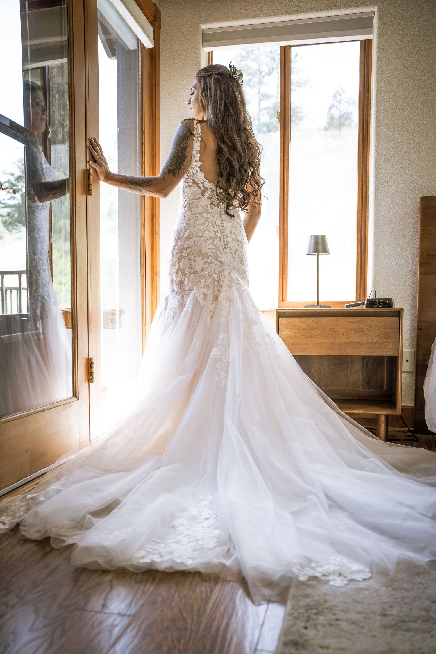 A stunning white lace wedding dress with long train shown in natural window light illuminating its intricate details.