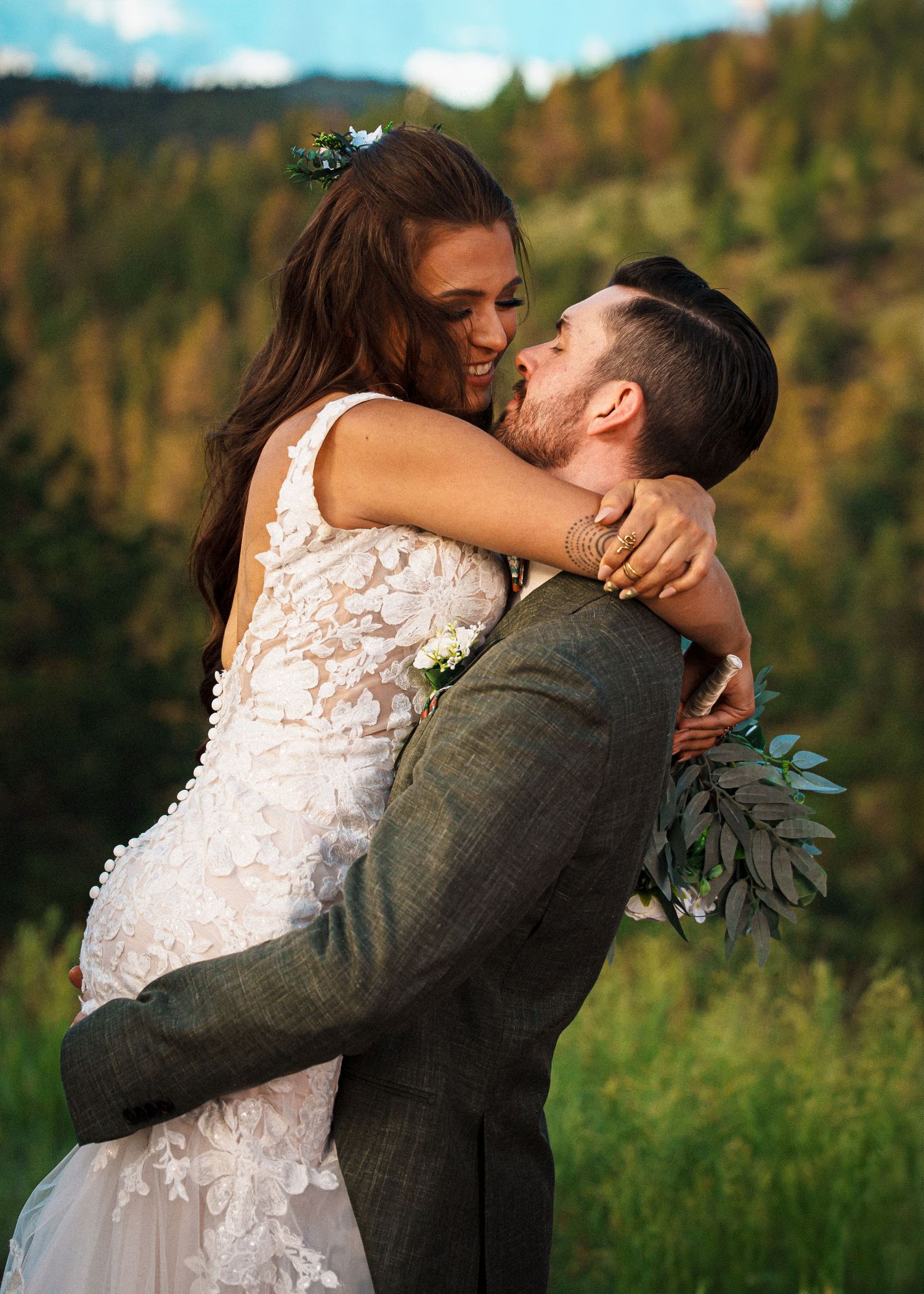 A romantic wedding moment captured at sunset in front of autumn mountain scenery, with a lace dress and grey suit.
