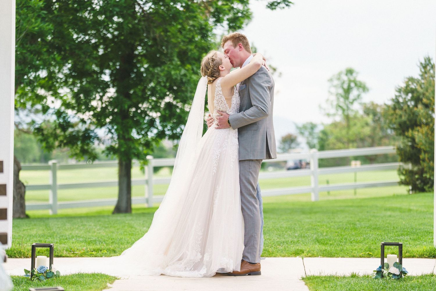 Romantic newlyweds share a tender kiss on a grassy hillside overlooking a scenic countryside view.