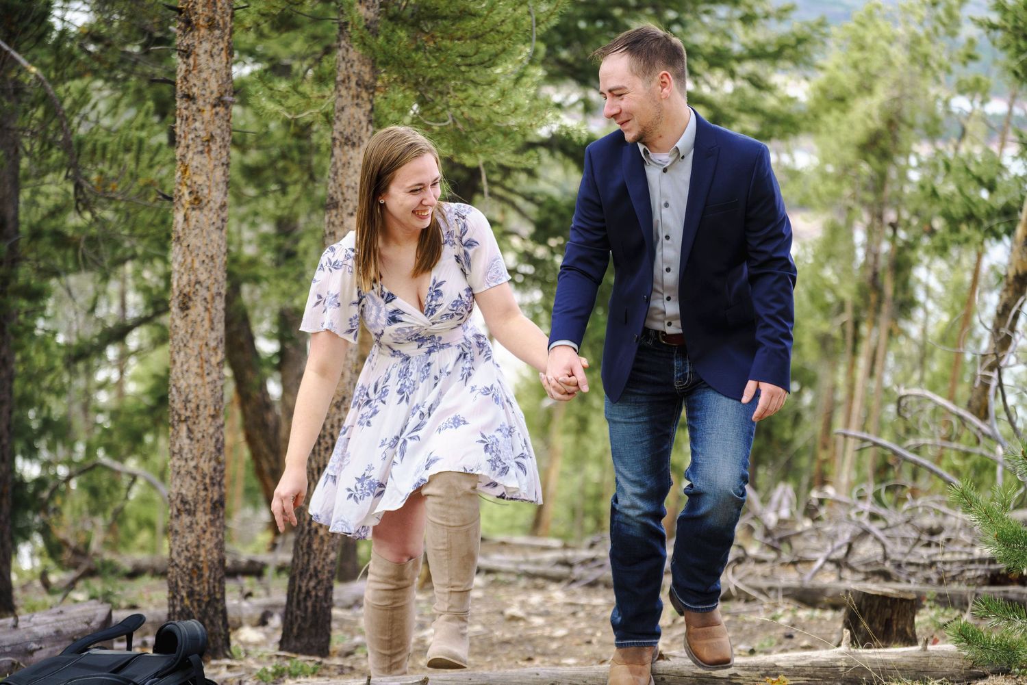A couple in casual attire holding hands while walking together along a wooded mountain trail in nature.