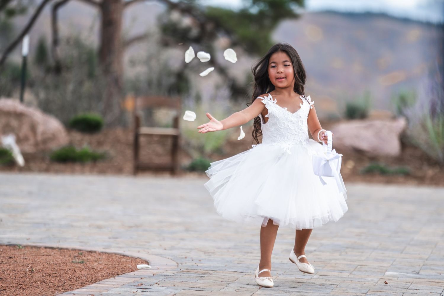 A young girl in a white tulle dress twirls joyfully with bubbles floating around her outdoors.