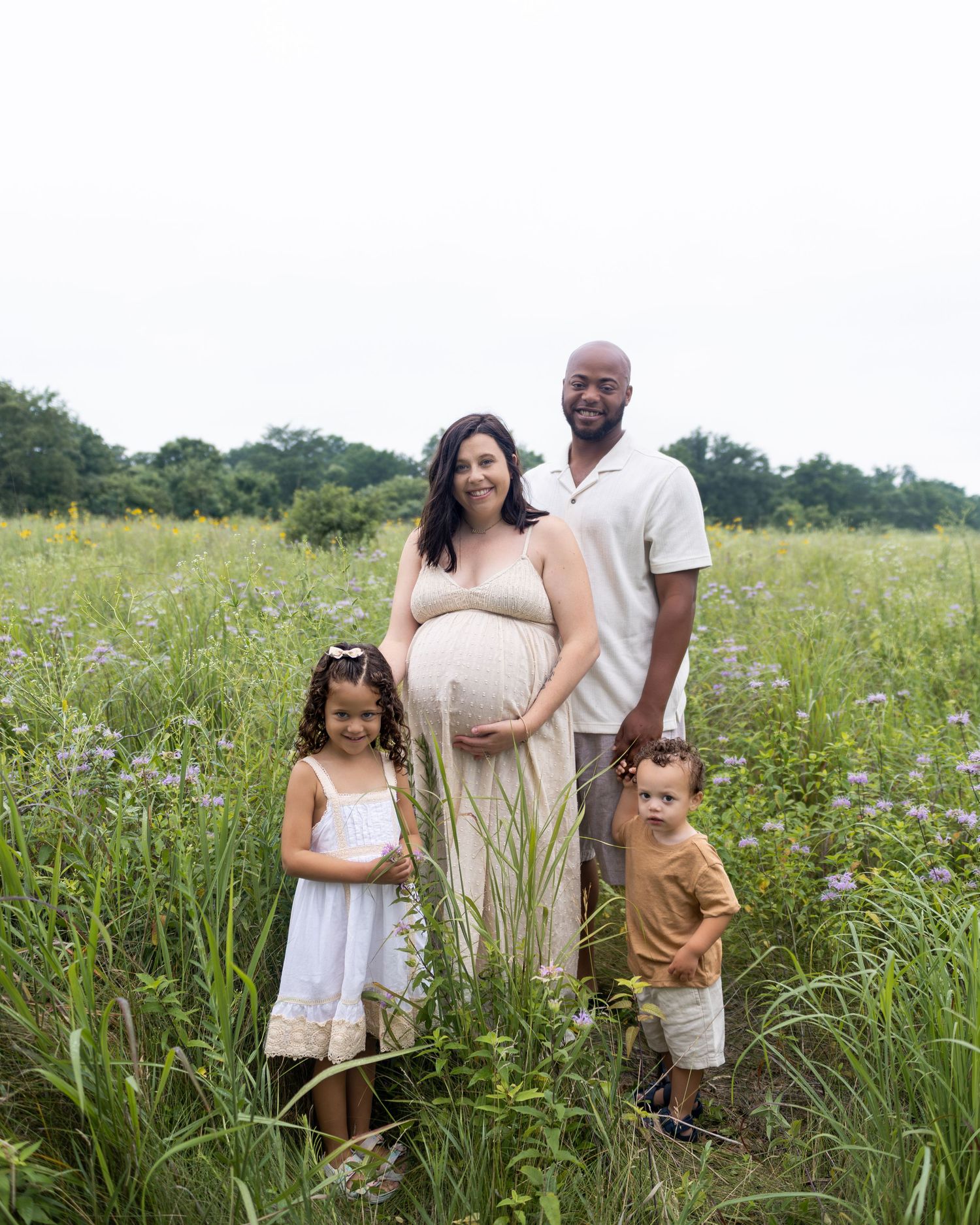 A family stands together in a scenic wildflower meadow on a bright summer day.