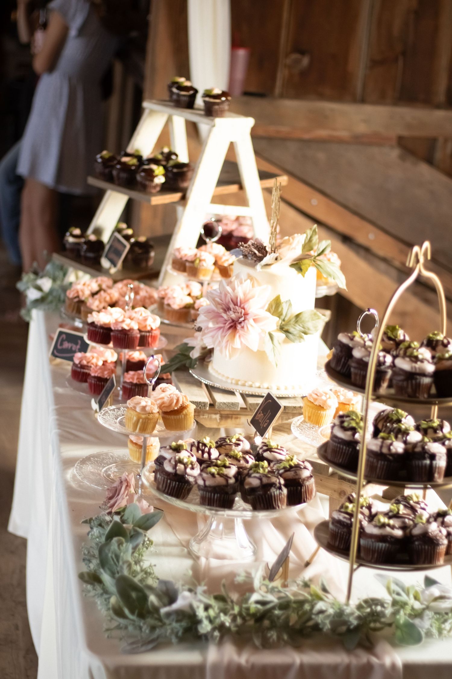 Elegant tiered dessert display with cupcakes and flowers at a wedding reception.