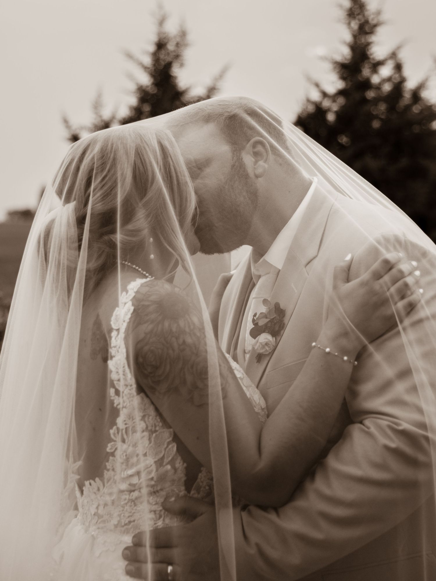 Romantic sepia-toned wedding photograph showing couple sharing an intimate kiss under a delicate veil.