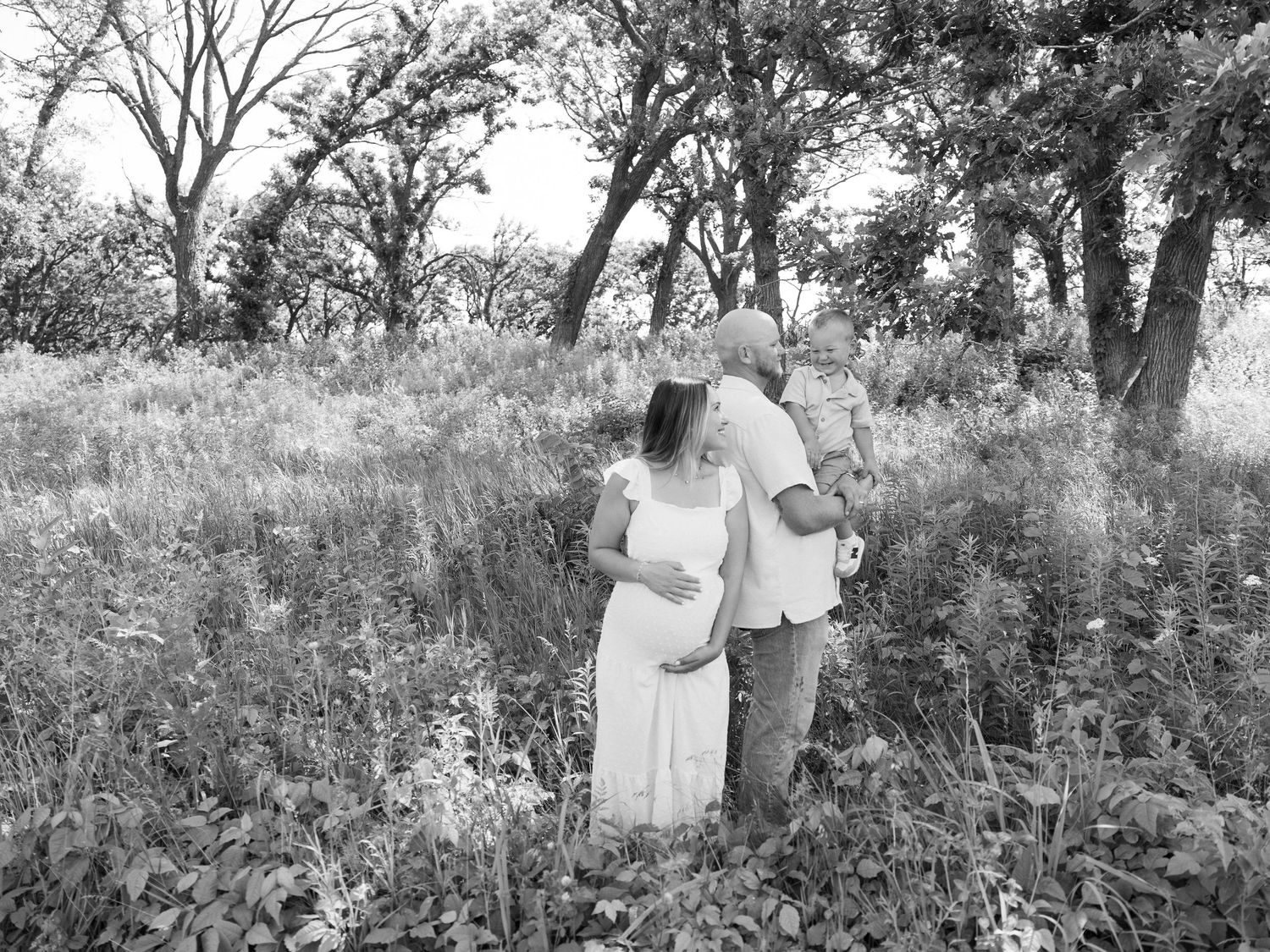 A couple embraces in a romantic black and white photo series set against a natural outdoor backdrop with trees and foliage.