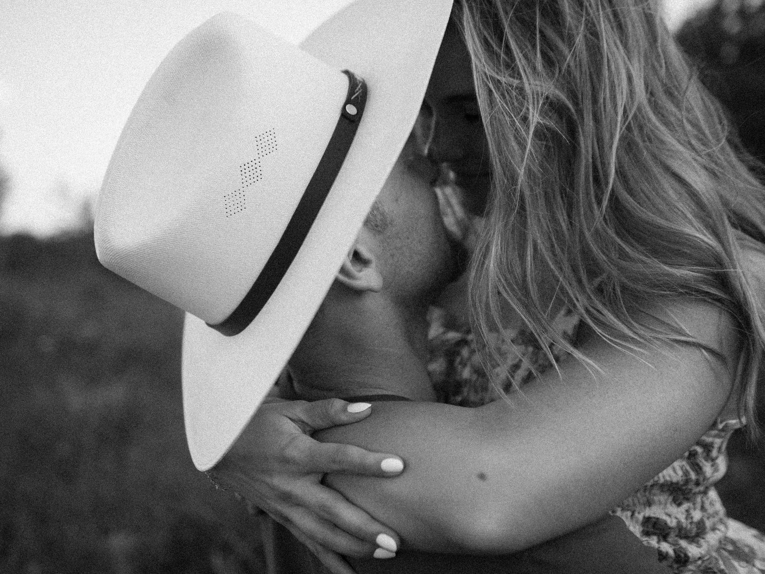 A romantic black and white photo showing a gentle kiss while wearing a white fedora hat.