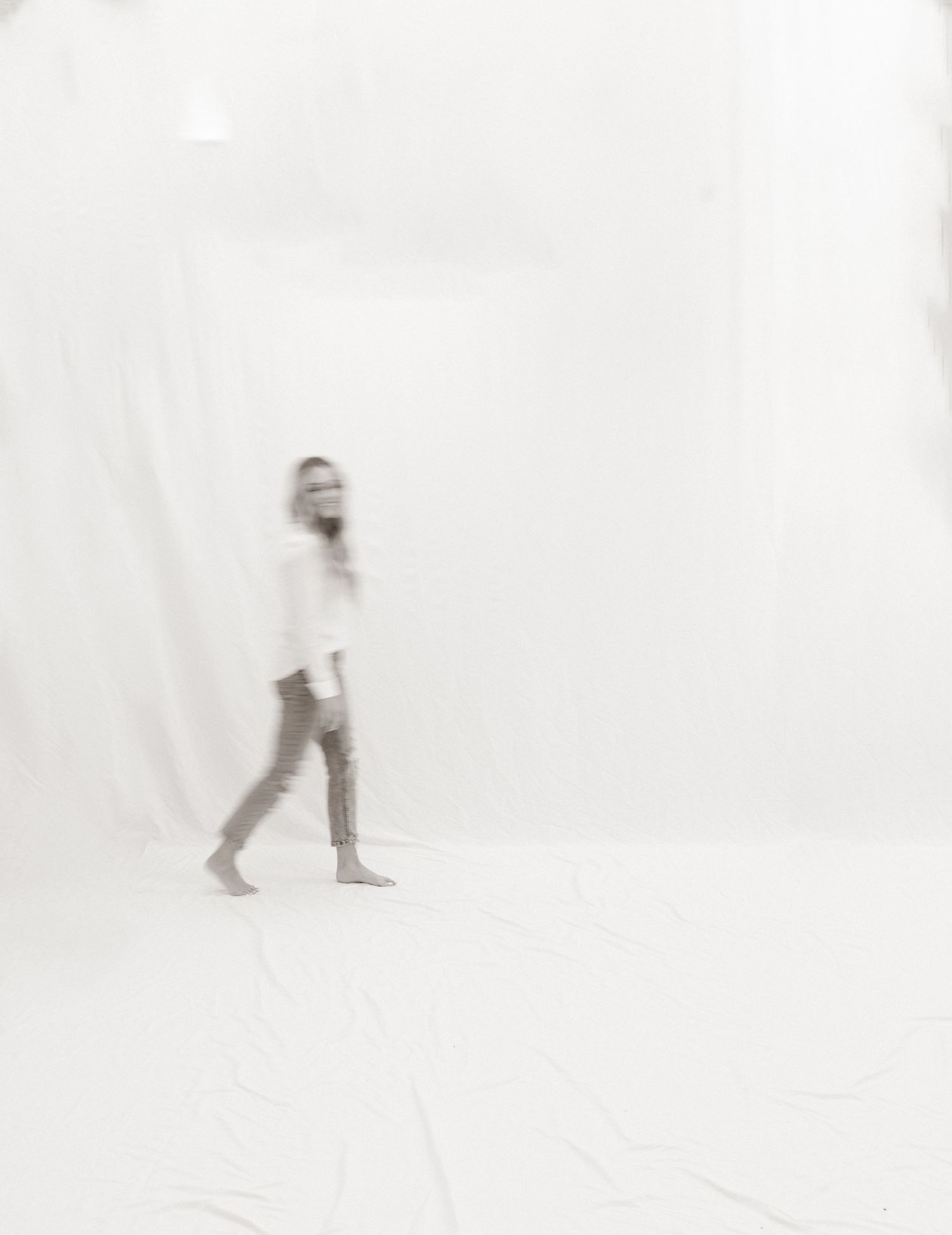 An artistic blurred black and white image of a person walking against a white background.